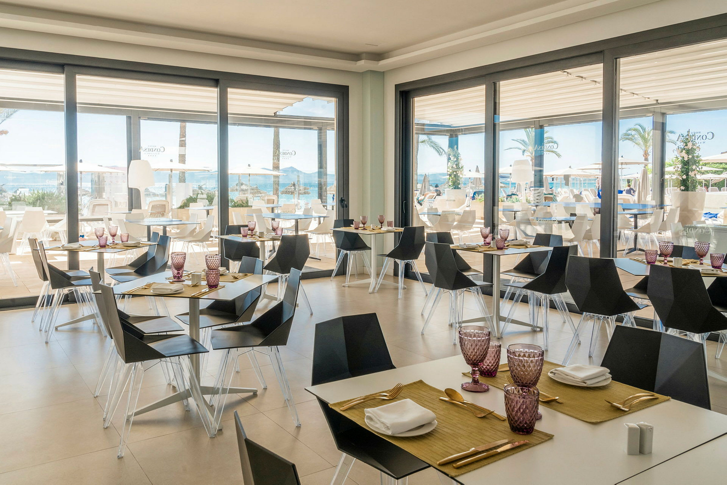 Restaurant med moderne møbler og dekkede bord ved store vinduer med utsikt mot basseng og hav. (AI-generert tekst)