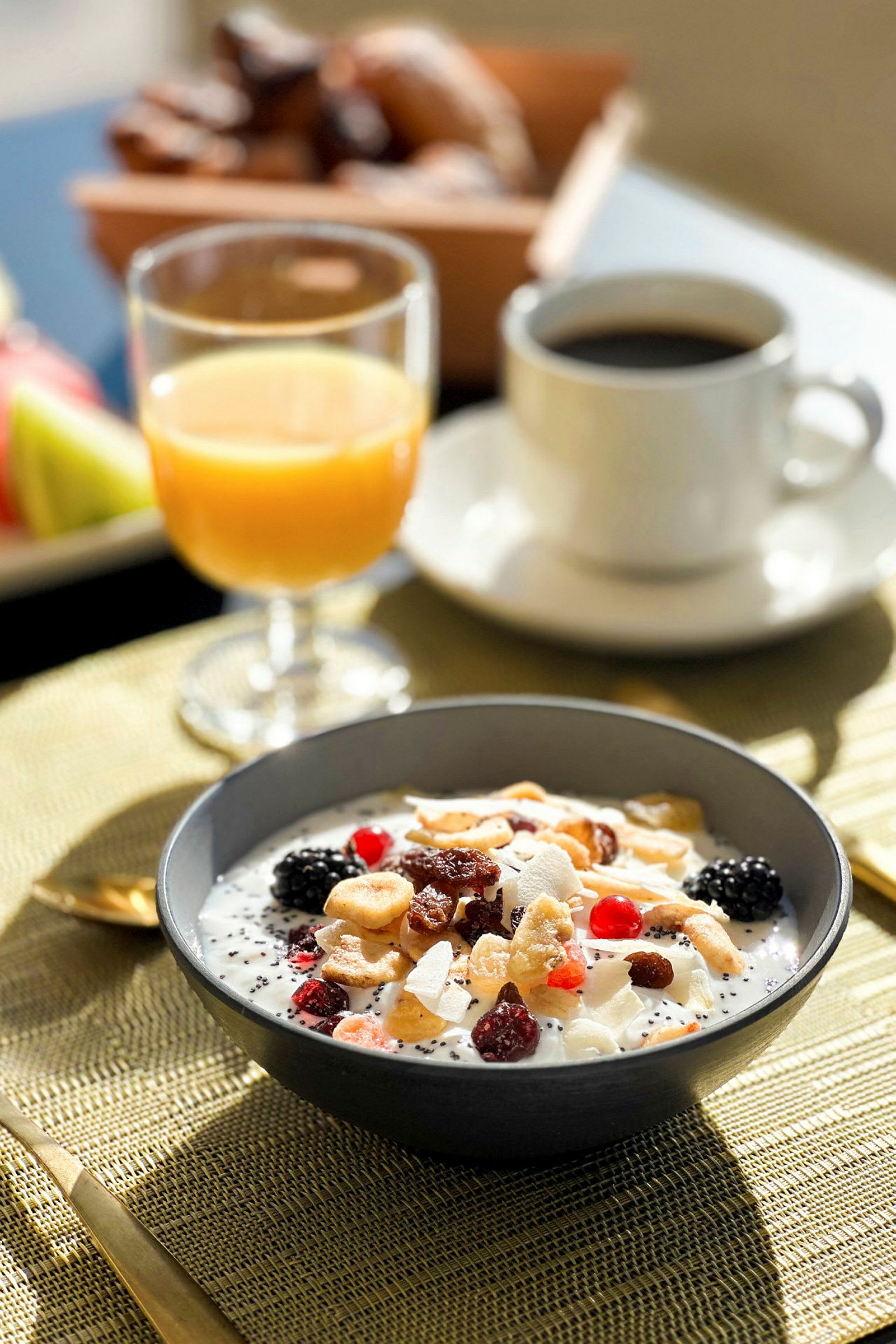 En frokostskål med yoghurt, frukt og nøtter ved siden av et glass appelsinjuice og en kopp kaffe. (AI-generert tekst)