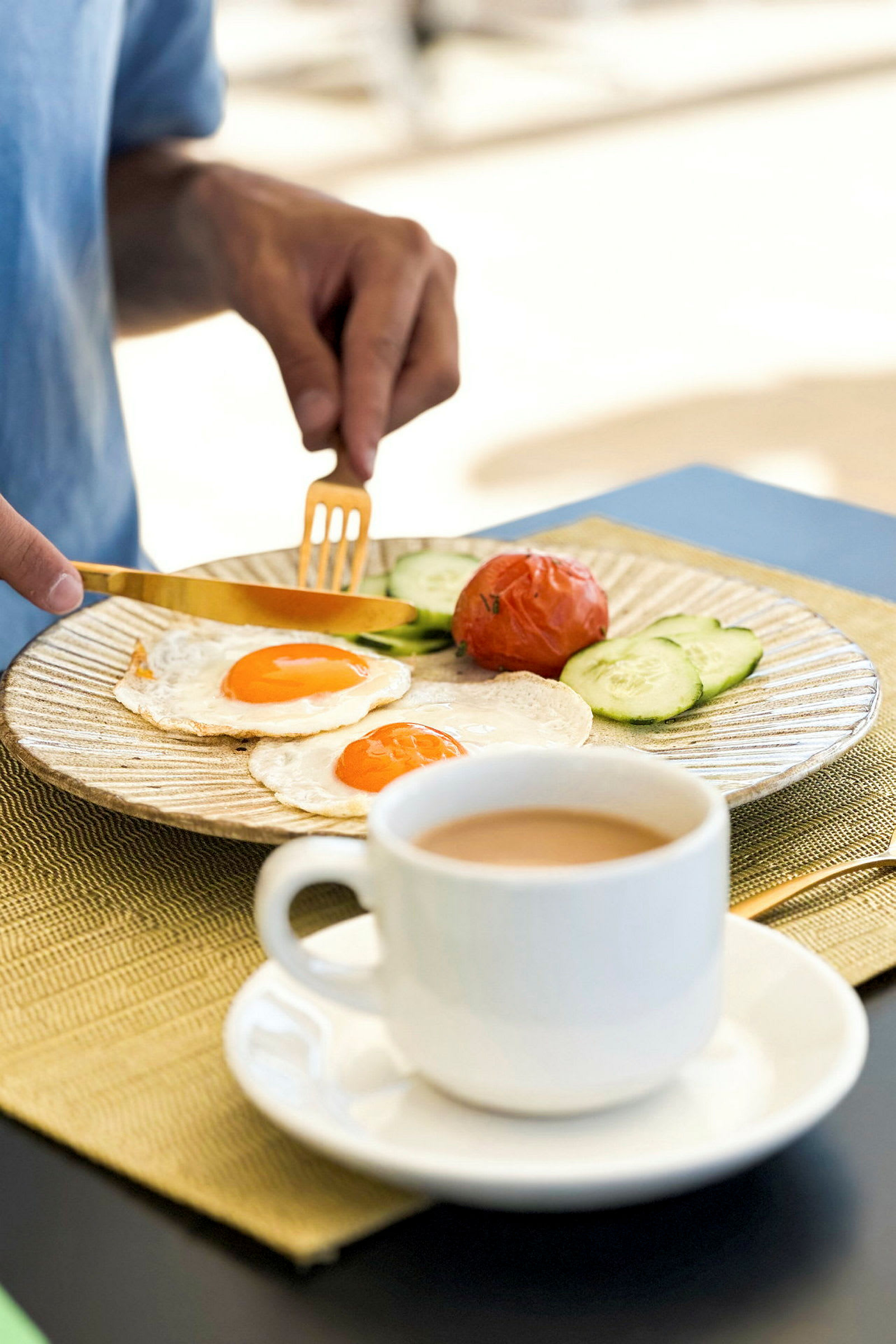 En person spiser frokost bestående av stekte egg, tomat, agurkskiver og kaffe. (AI-generert tekst)