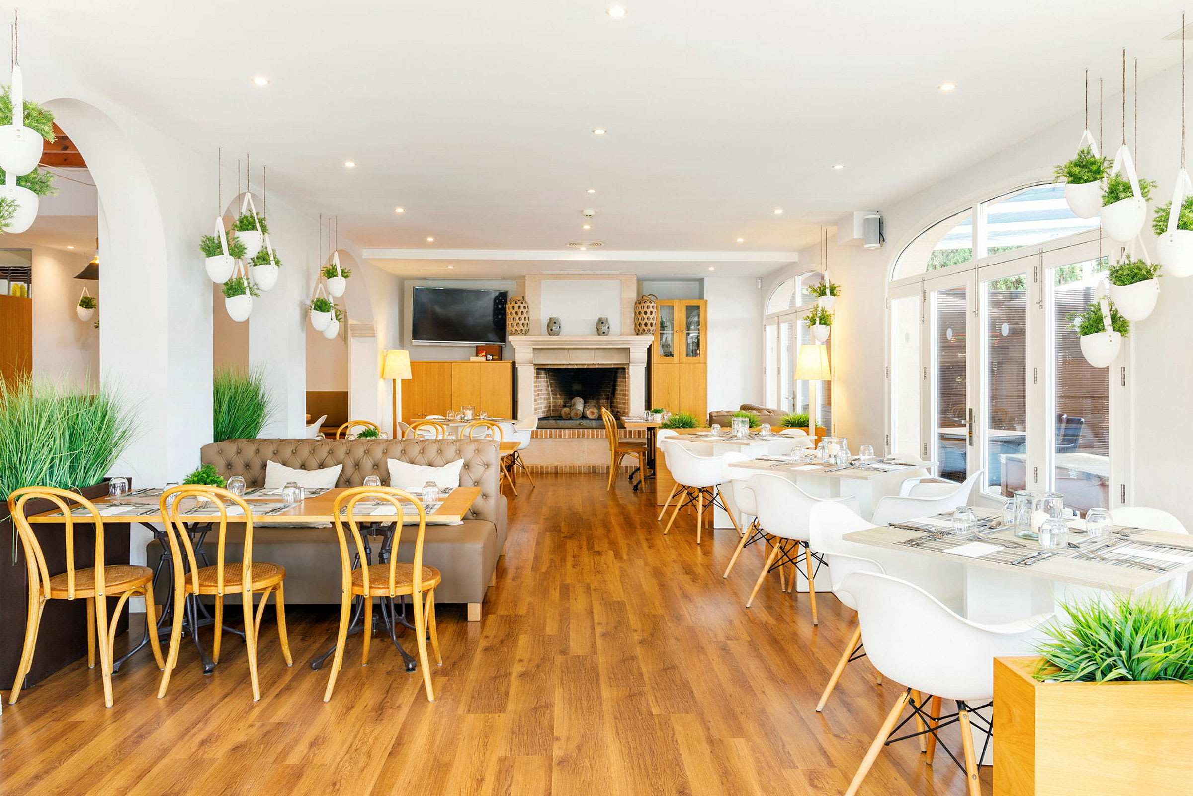 En lys restaurant med moderne møbler og hvite bord omgitt av grønne planter. (AI-generert tekst)