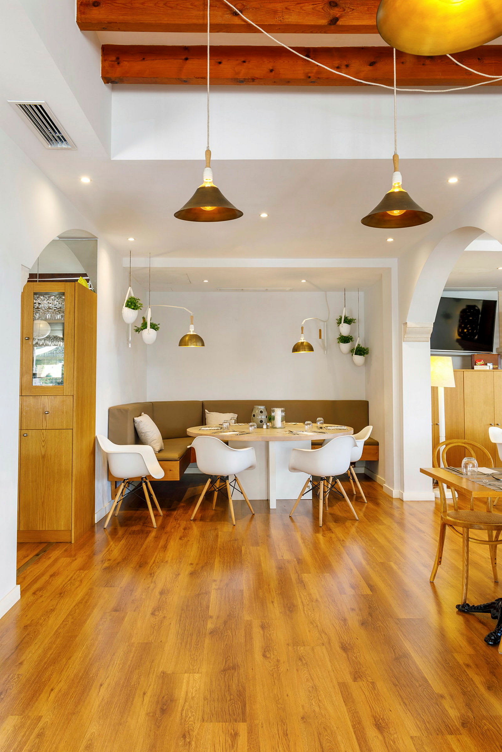 Et moderne restaurantinteriør med tregulv, et bord med stoler og sofaer, og hengende lamper. (AI-generert tekst)