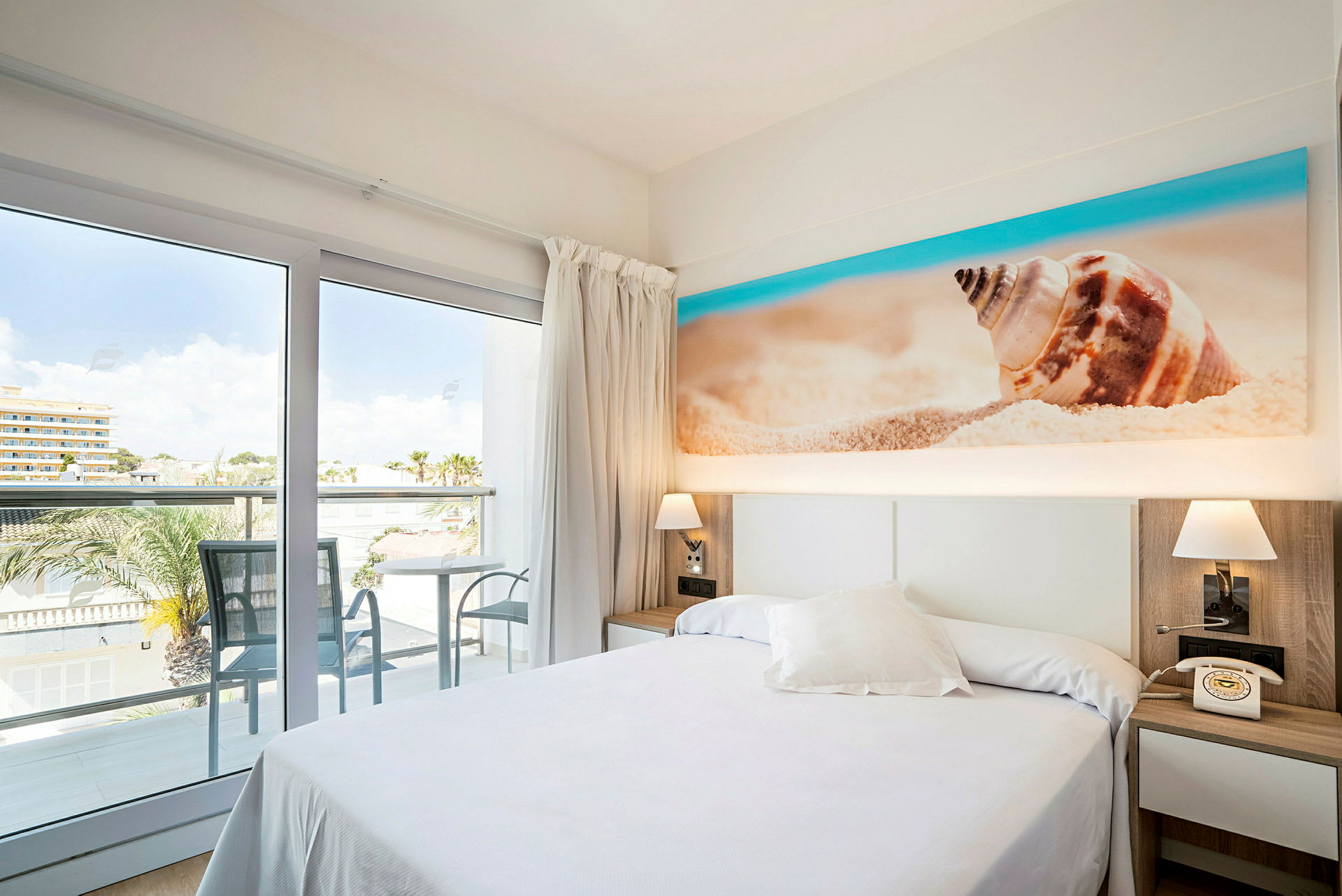 Hotellrom med balkong og utsikt, seng og dekorasjon med strandmotiv. (AI-generert tekst)