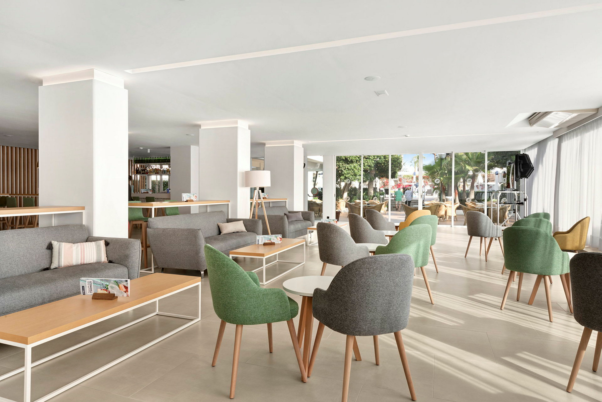 En lys og moderne lounge med grønne og grå stoler, bord og store vinduer. (AI-generert tekst)