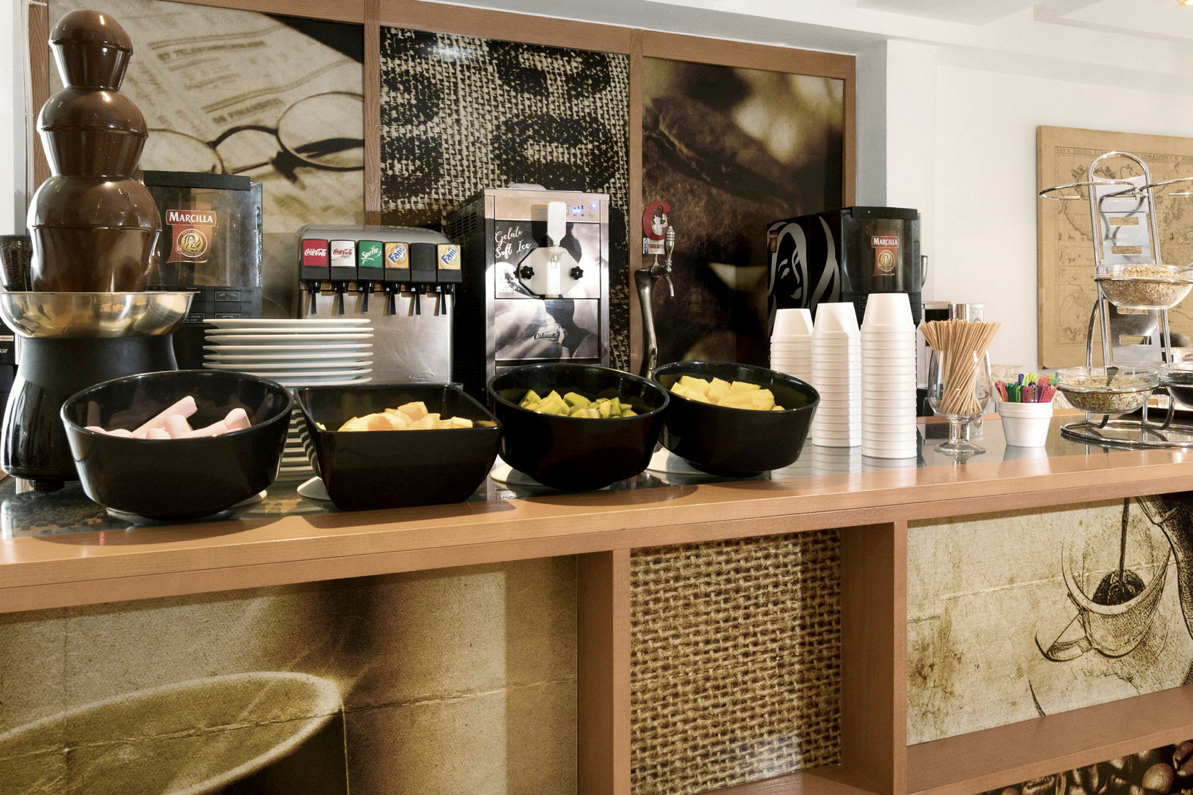 En selvbetjeningsdisk med sjokoladefontene, frukt, drikkevarer og kaffekopper. (AI-generert tekst)