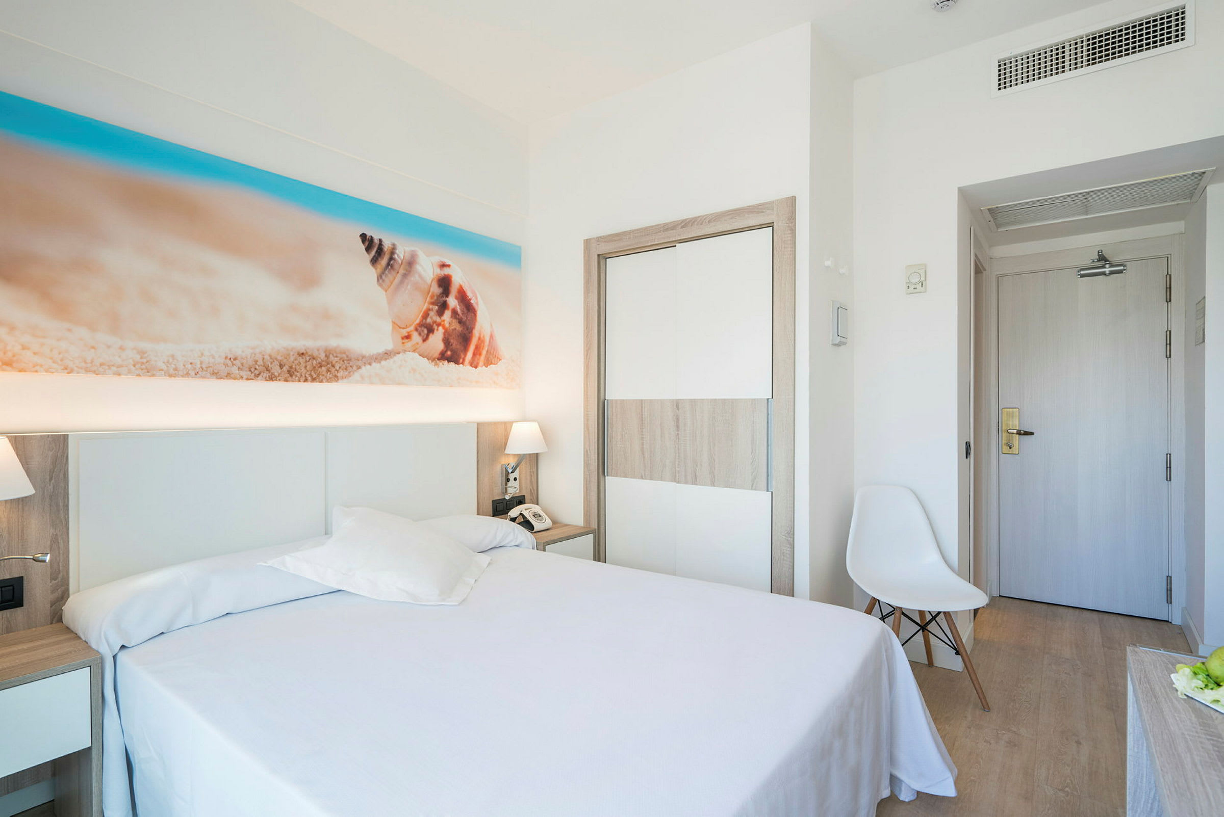 Et hotellrom med en dobbeltseng og strandinspirert kunstverk på veggen. (AI-generert tekst)