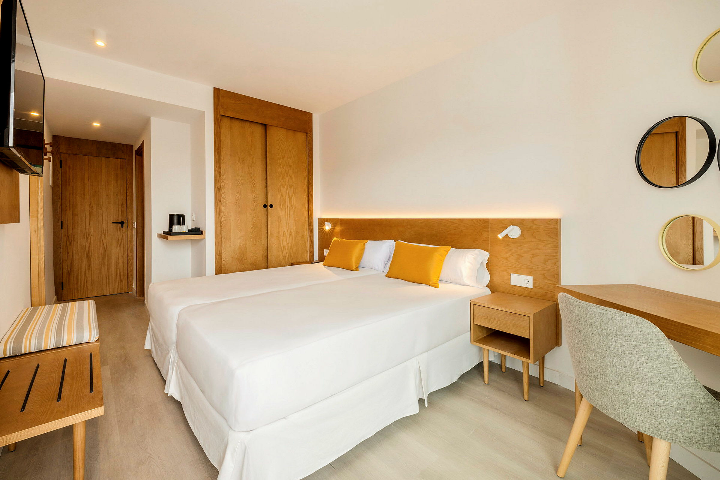 Et lyst og moderne innredet hotellrom med to enkeltsenger, tremøbler og gulldetaljer i tekstiler. (AI-generert tekst)