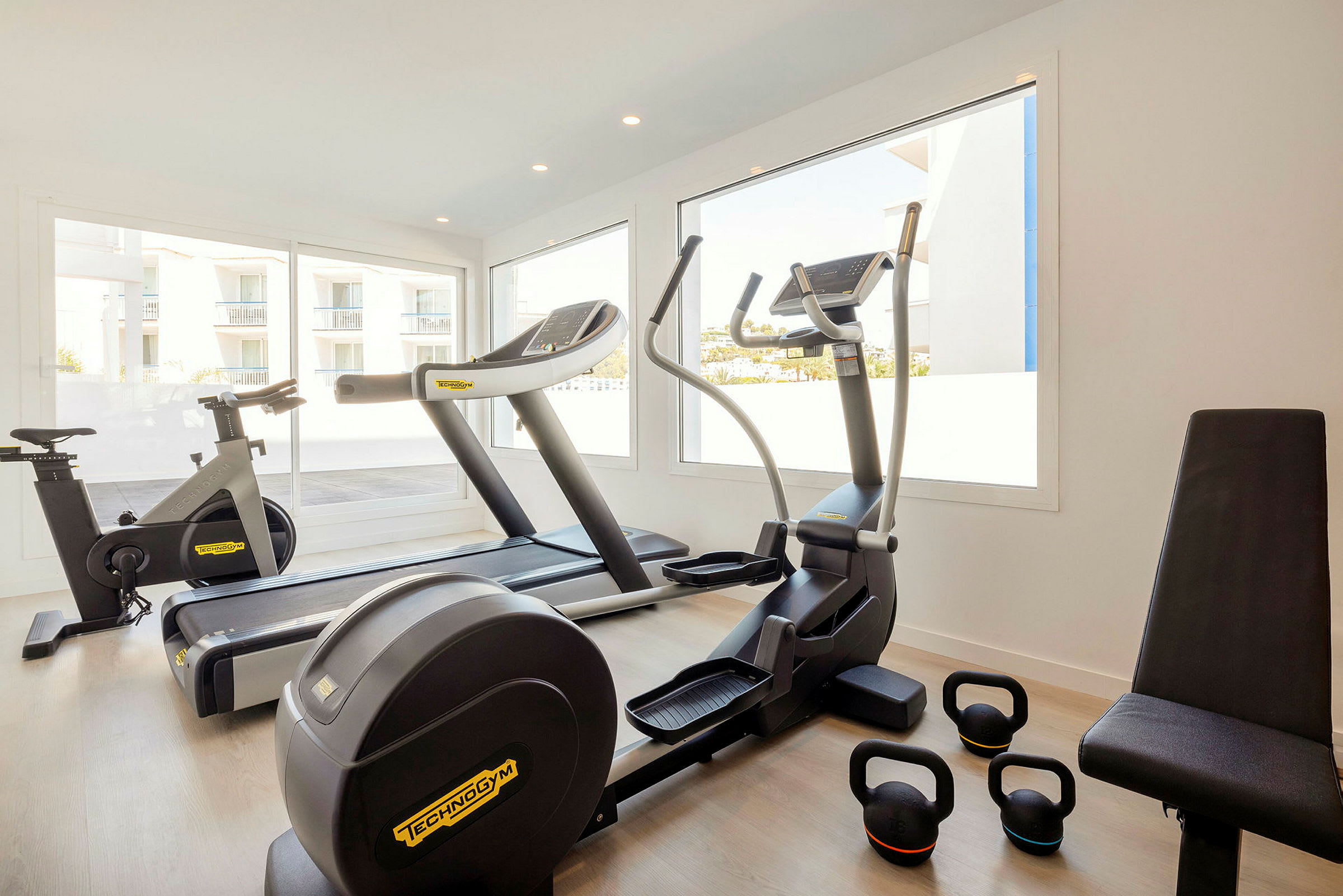 Ett treningsstudio med utstyr som sykkel, tredemølle, ellipsemaskin og kettlebells. (AI-generert tekst)