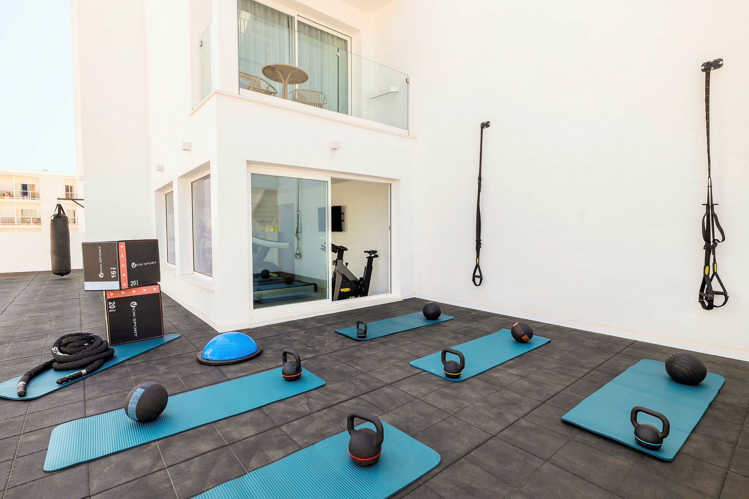 En utendørs treningsområde med treningsmatter, kettlebells, medisinballer og TRX-stropper samt en boksebag. (AI-generert tekst)