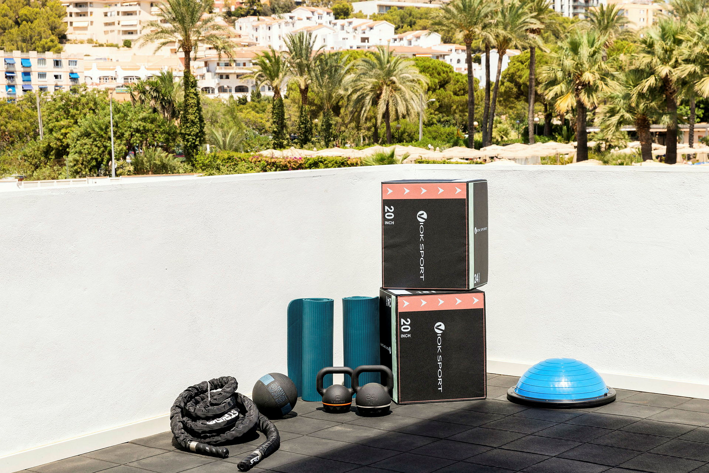Treningsutstyr inkludert bokser, treningsmatter, kettlebells og en balanseball på en uteplass. (AI-generert tekst)