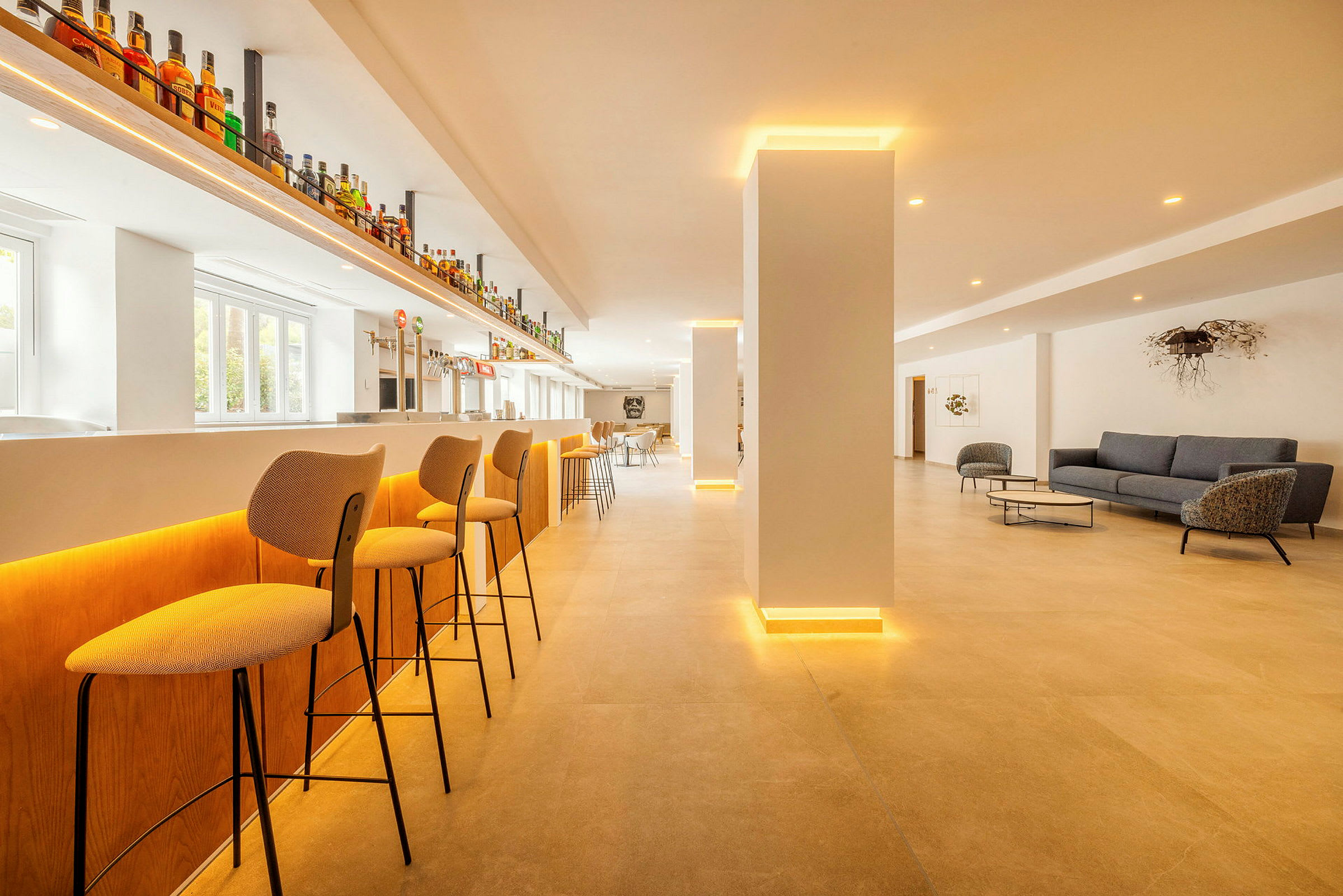 En moderne bar med høye stoler, lys innredning og en loungeområde med sofaer og bord. (AI-generert tekst)