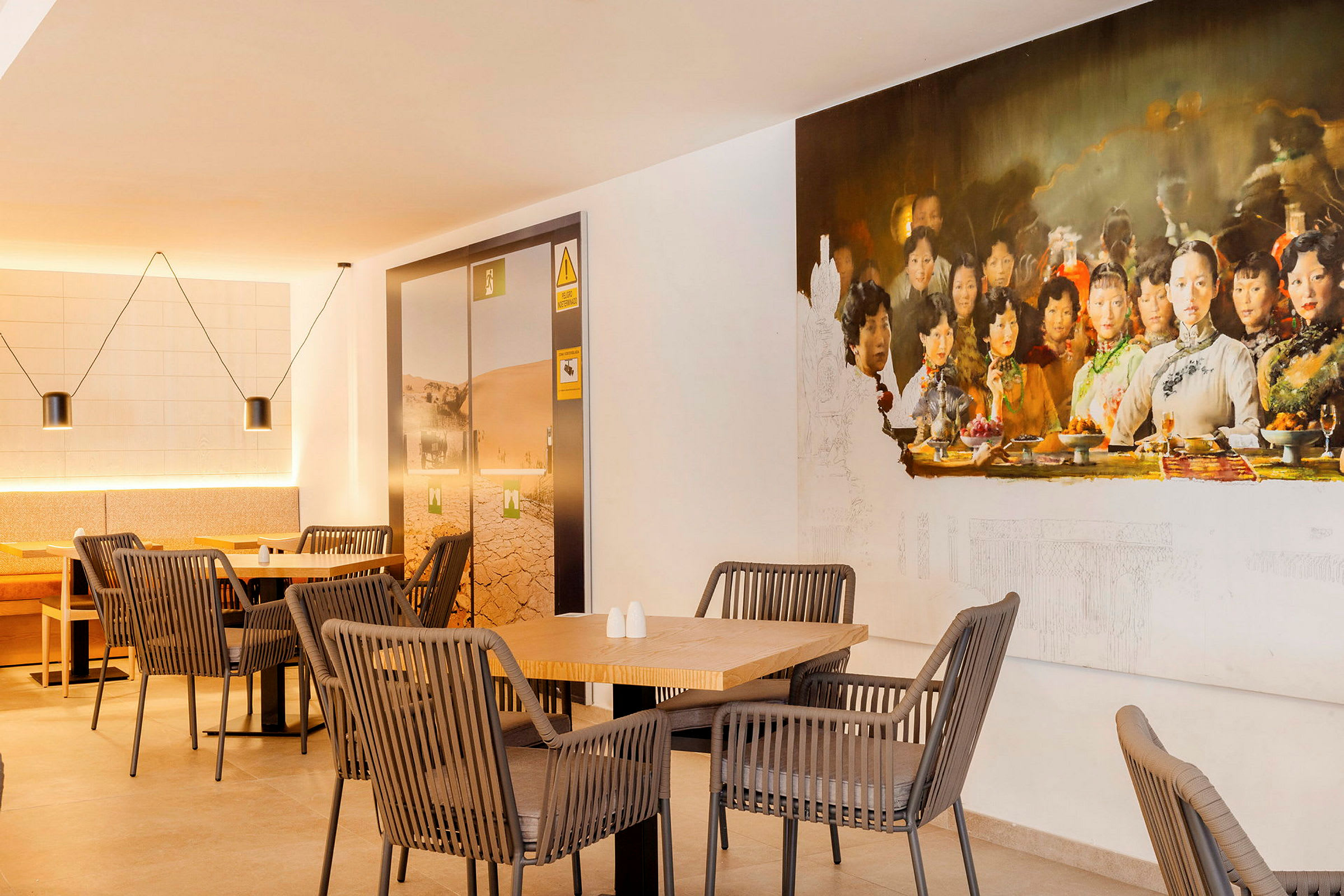 En innendørs kafé med moderne møbler og et stort veggmaleri som viser en gruppe mennesker ved et bord. (AI-generert tekst)
