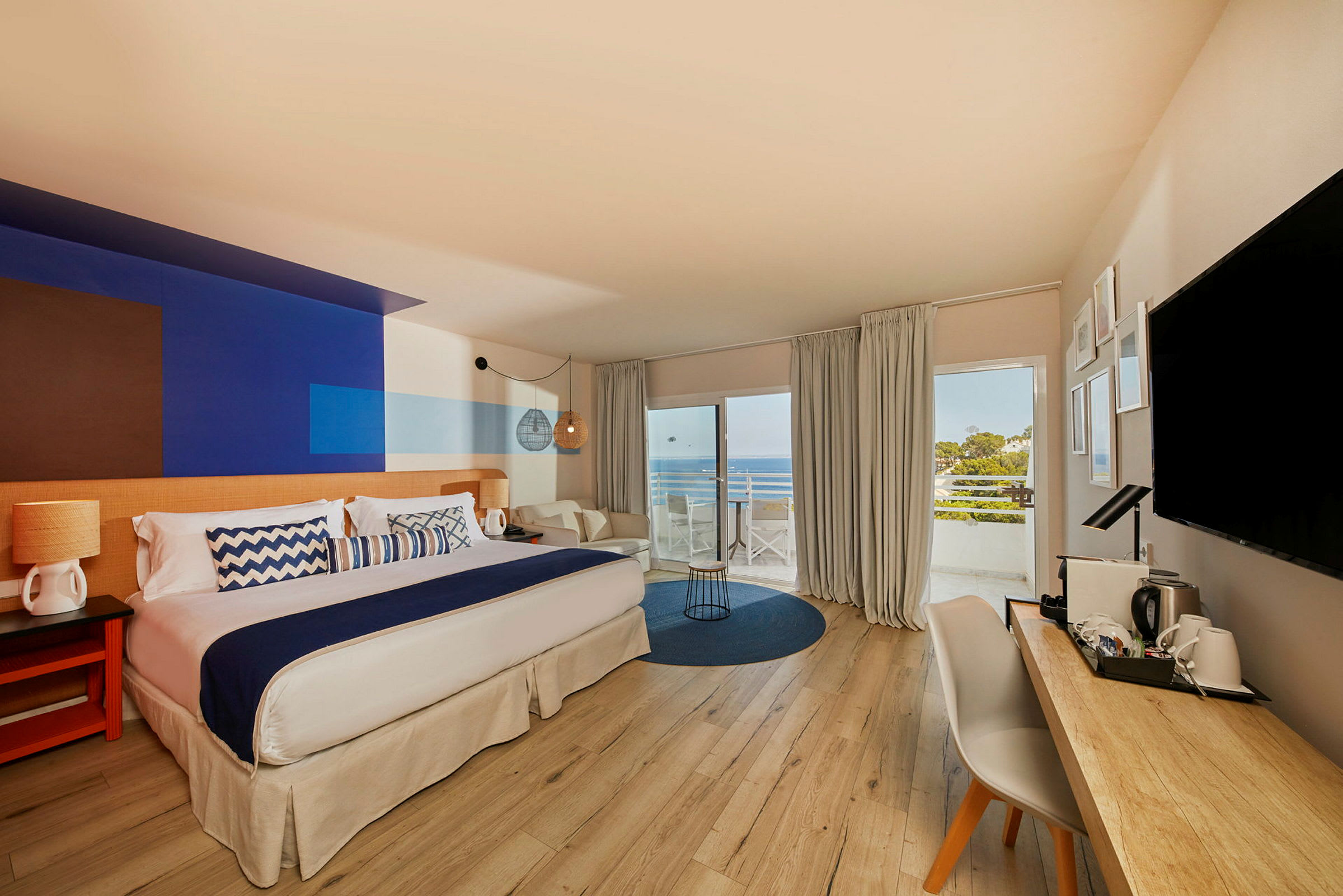 Et hotellrom med stor seng, skrivebord og utsikt over havet fra balkong. (AI-generert tekst)