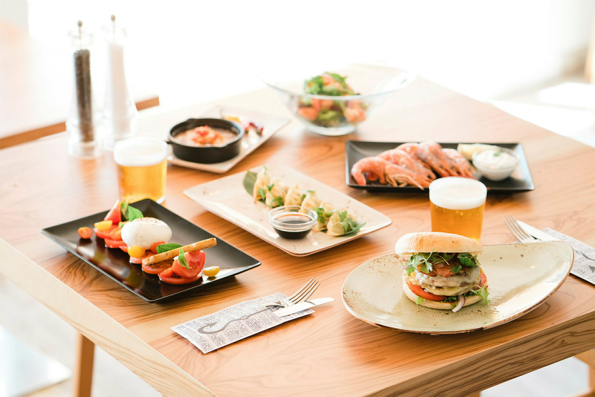 Et bord med forskjellige retter og drikkevarer, inkludert salat, reker, burger og øl. (AI-generert tekst)