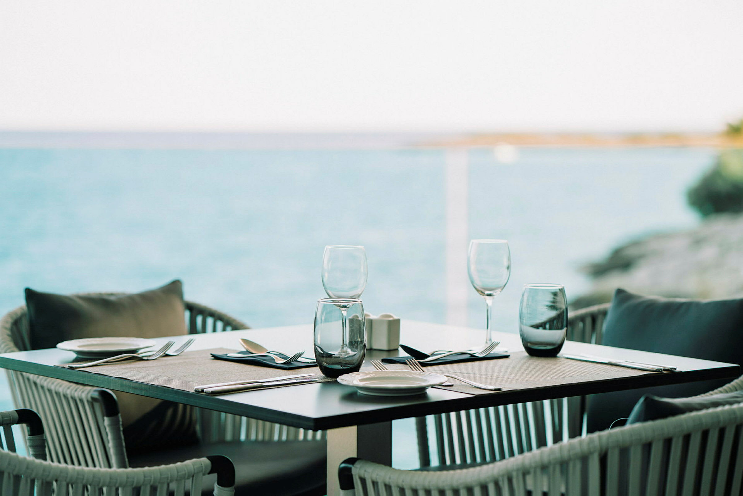 Et dekket bord med glass og bestikk ved havet. (AI-generert tekst)