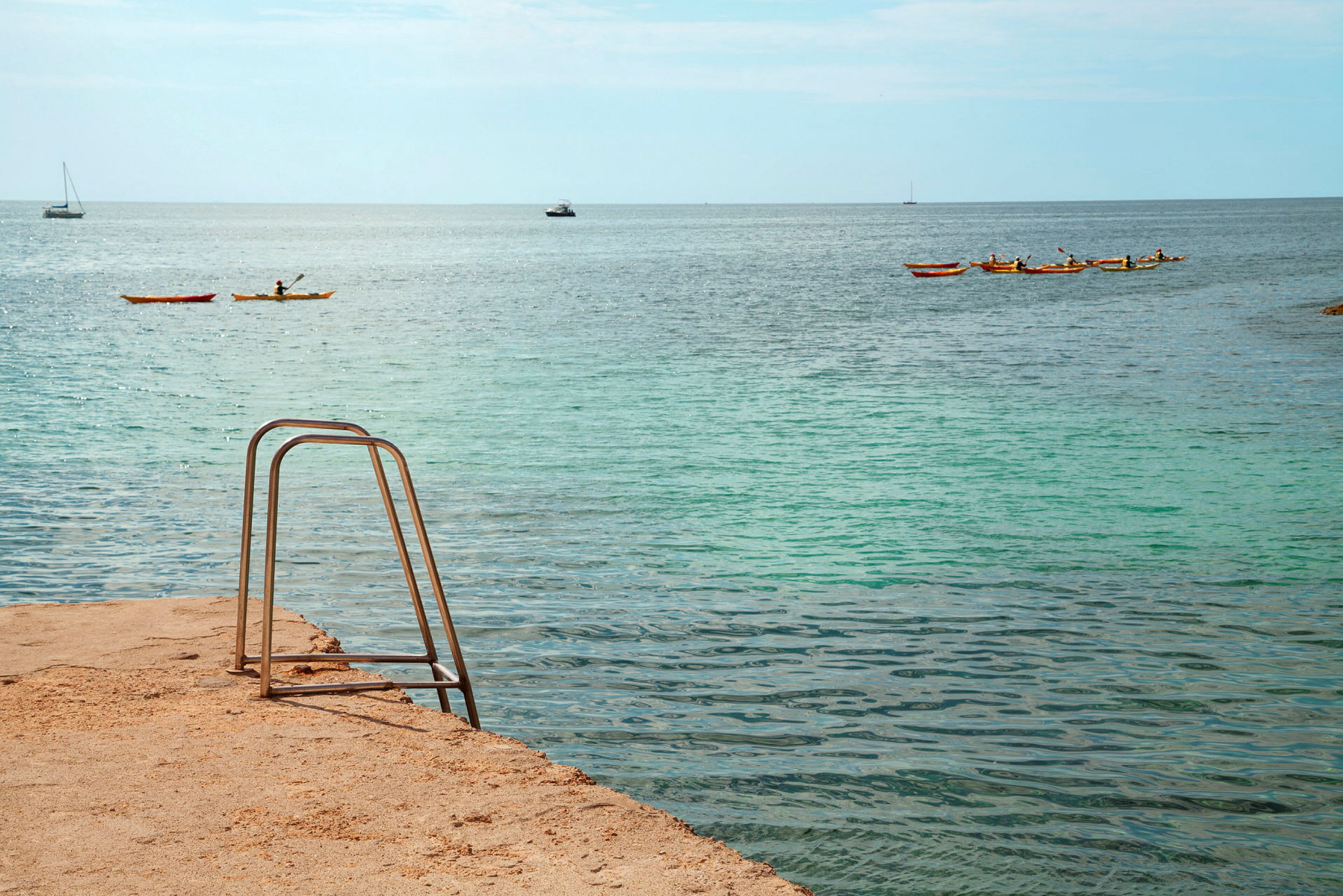 En badestige ved havet, med kajakker og båter på vannet. (AI-generert tekst)