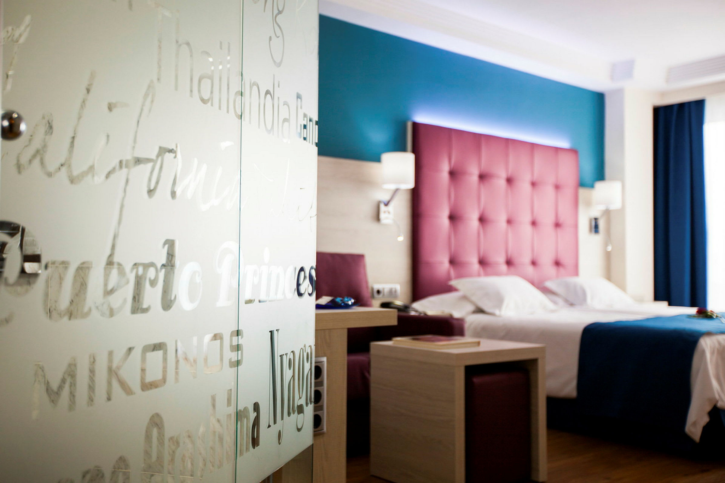 Hotellrom med fargerik innredning, seng og bord. (AI-generert tekst)