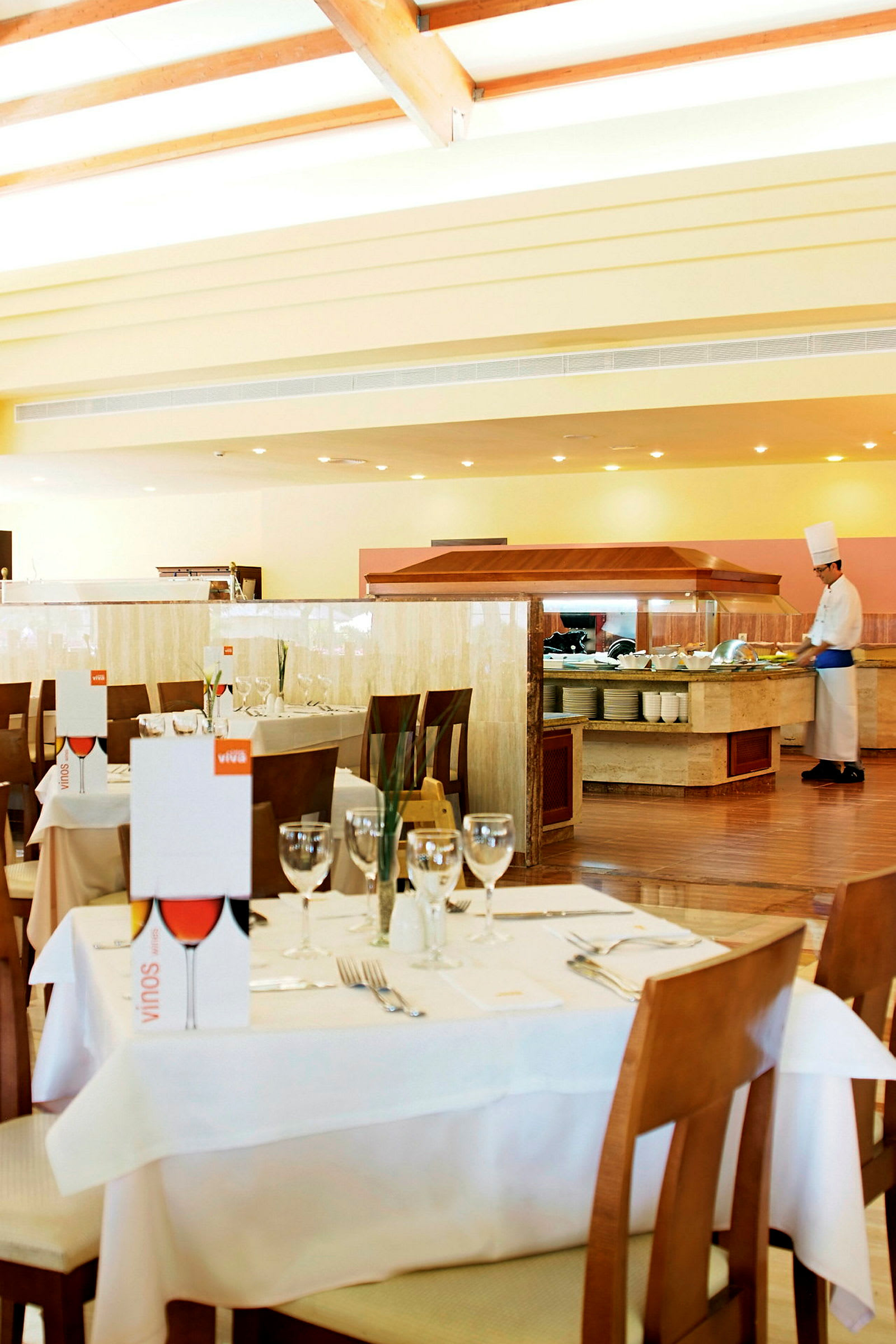 En restaurant med dekkede bord og en bufféstasjon hvor en kokk arbeider. (AI-generert tekst)