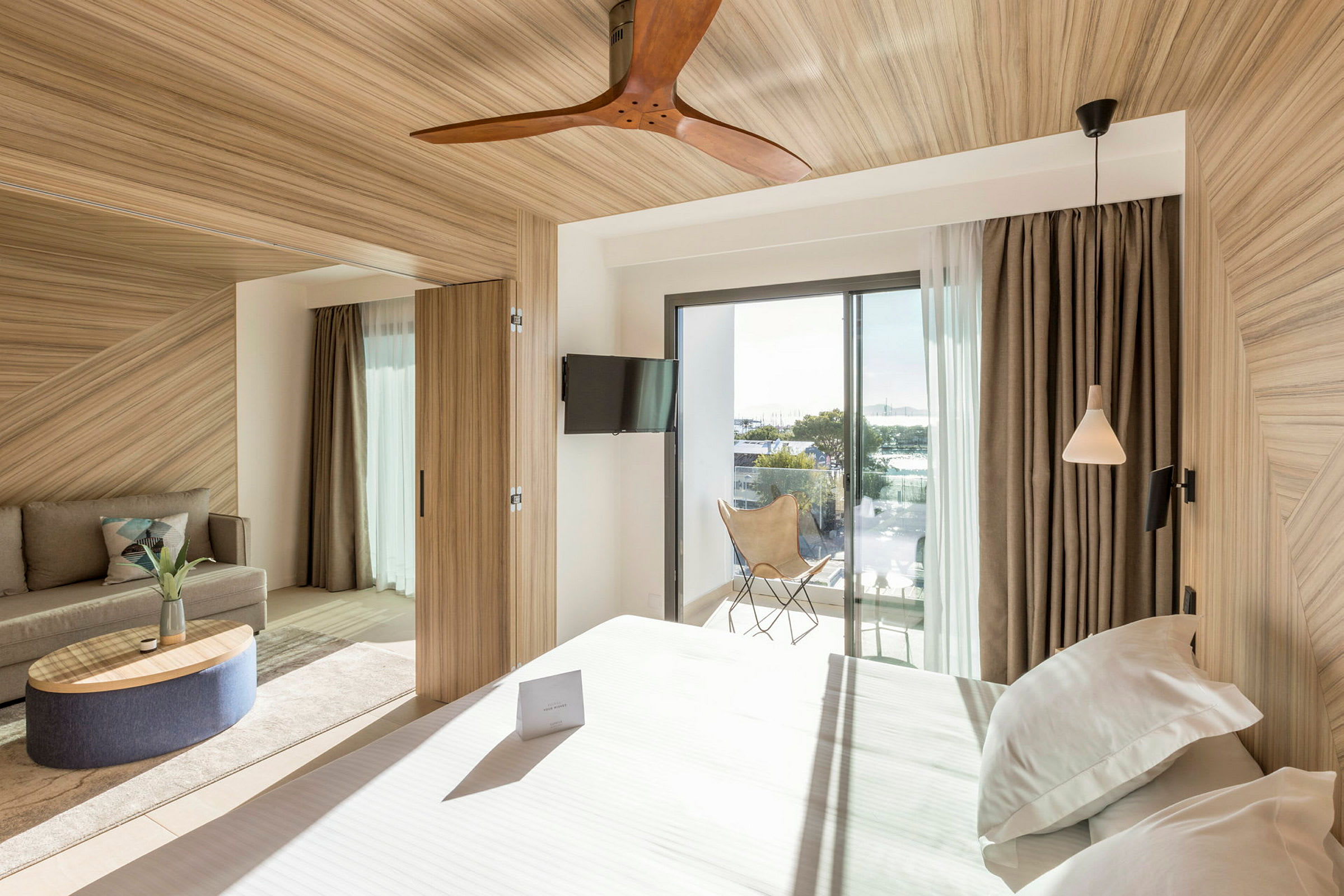 Et hotellrom med moderne interiør, seng, sofa og en balkong med glassdører. (AI-generert tekst)
