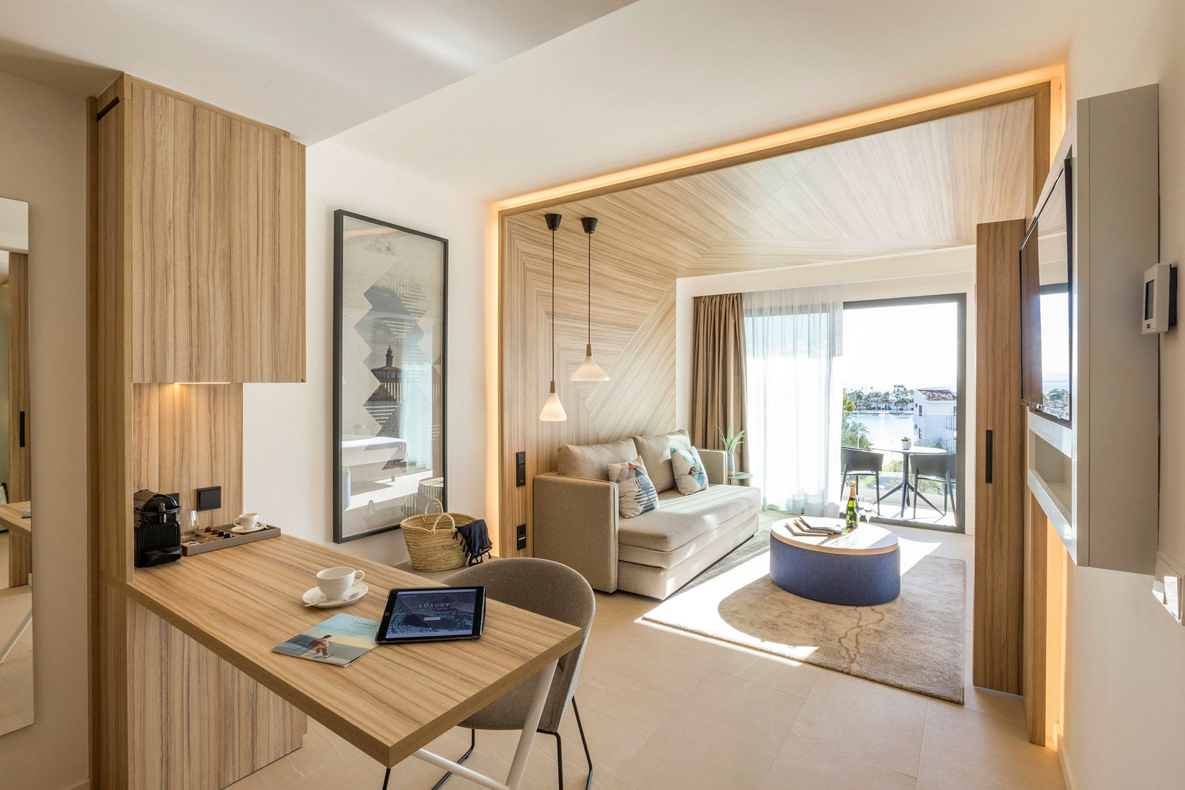 Et moderne hotellrom med tredetaljer, en sittegruppe og et lite bord på et teppe. Balkongen har utsikt over en hage og vannet utenfor. (AI-generert tekst)