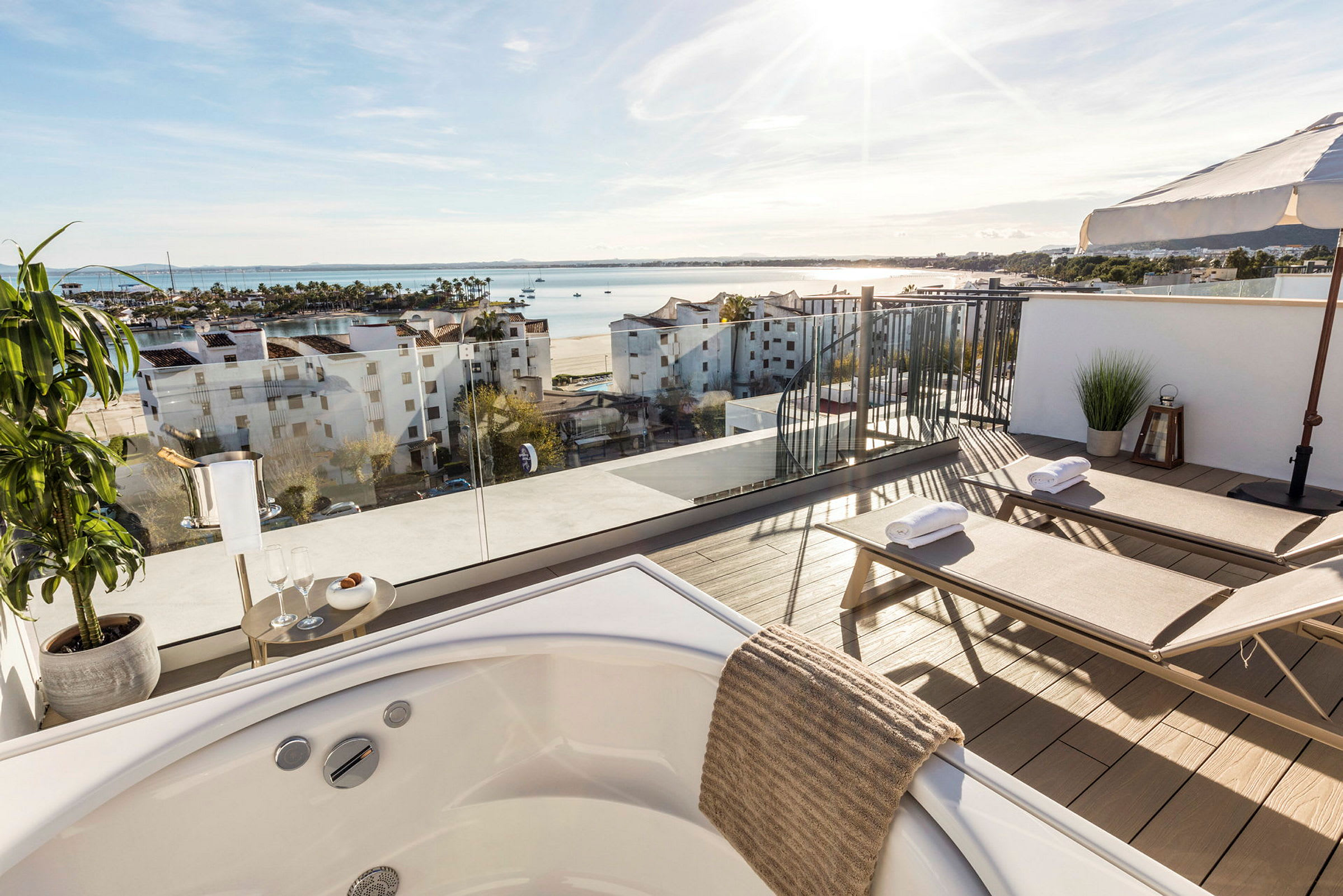 En terrasse med utsikt over havet, møblert med to solsenger og et bord. Det er også et boblebad i forgrunnen. (AI-generert tekst)