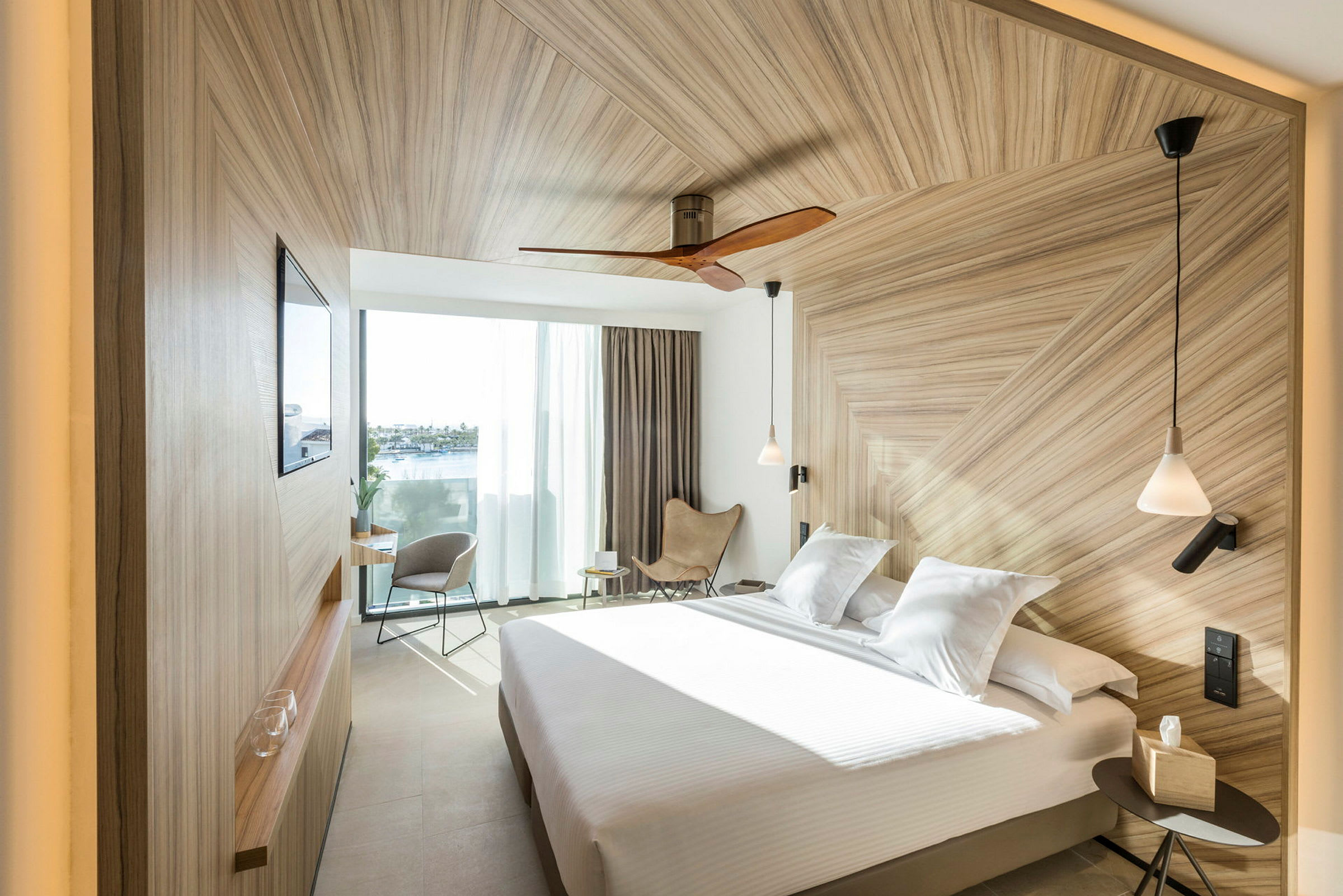Et moderne hotellrom med en stor seng, elegant trepanel, og store vinduer som slipper inn dagslys. (AI-generert tekst)