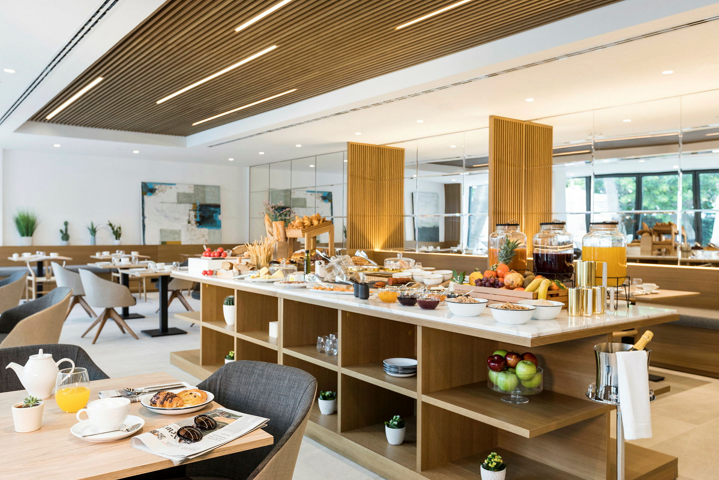 Bilde av en frokostbuffé med bord fylt med forskjellige matvarer og drikkevarer i en lys og moderne spisesal. (AI-generert tekst)