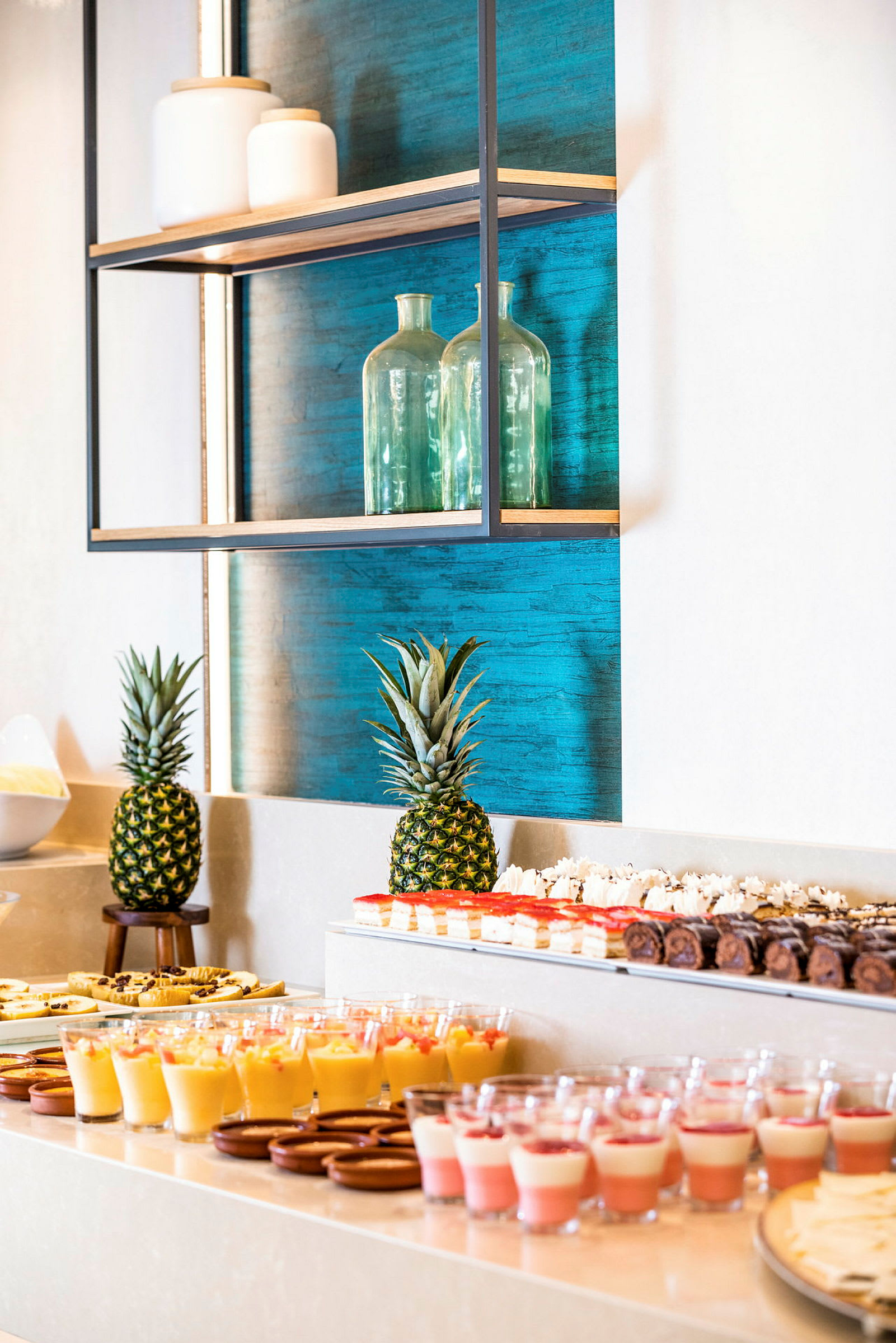 Et bord med desserter og to ananas foran en blå bakgrunn. (AI-generert tekst)
