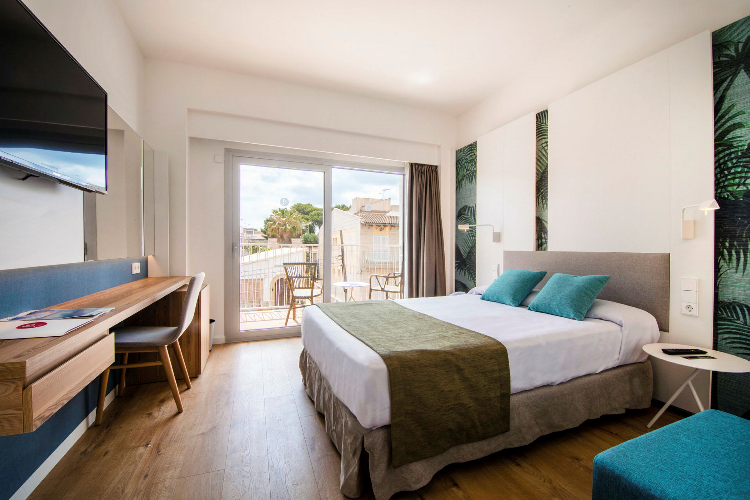 Et lys og moderne hotellrom med en stor seng, skrivebord, TV og en balkong med sittemøbler. (AI-generert tekst)