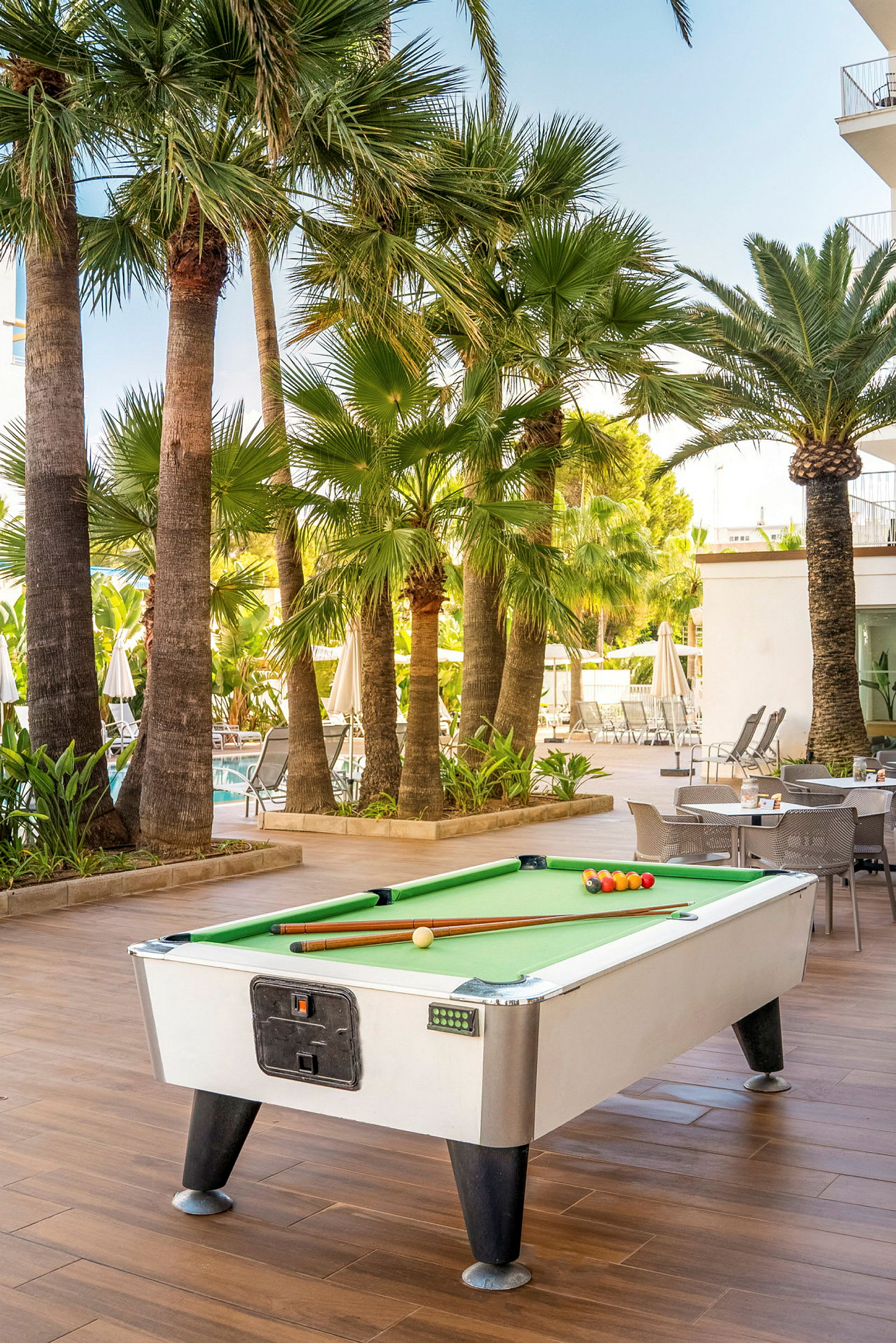 Et biljardbord står utendørs på en terrasse omgitt av palmer. (AI-generert tekst)