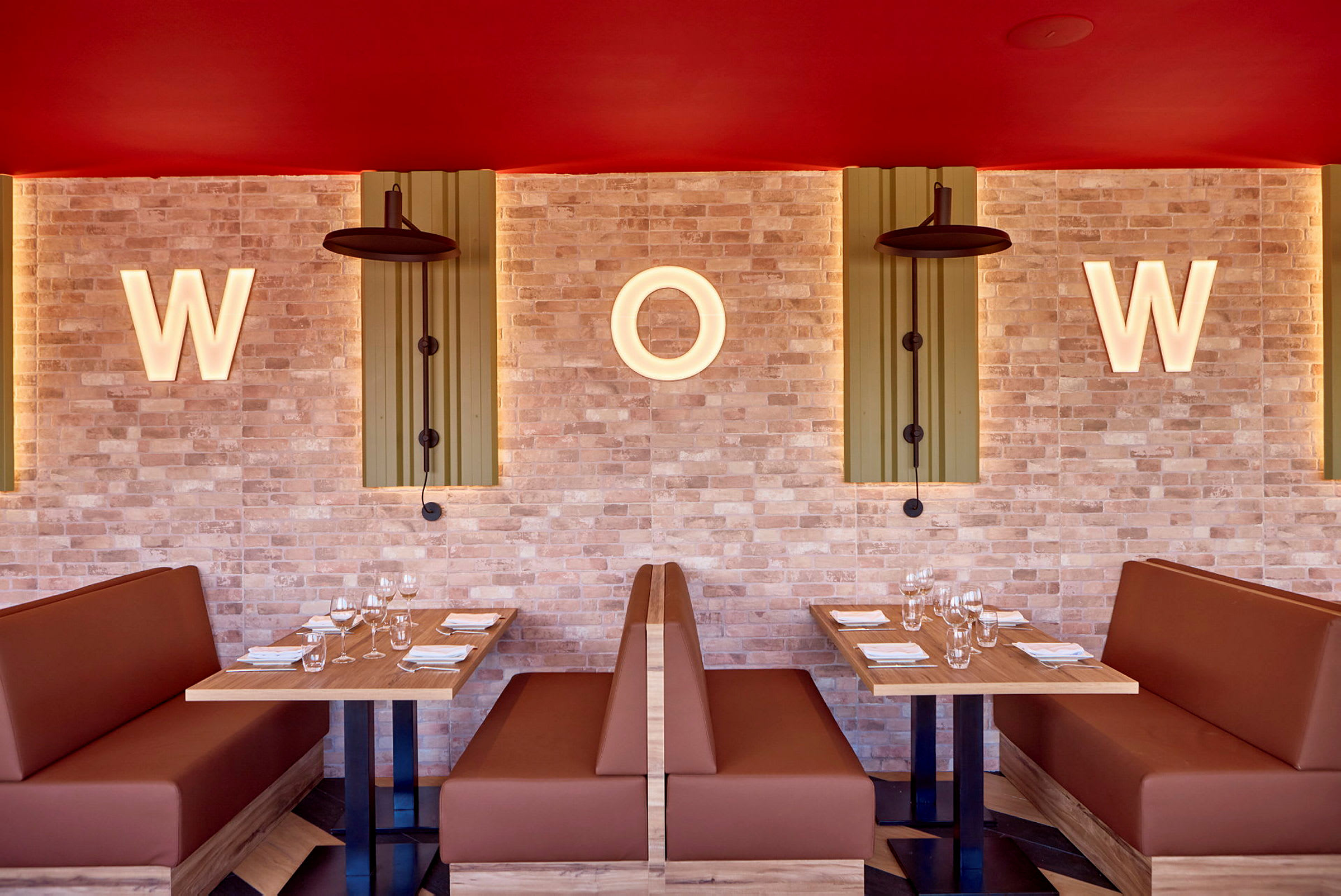 To sitteplasser med bord og sofaer i en restaurant, med opplyste bokstaver "W" og "O" på en murvegg. (AI-generert tekst)