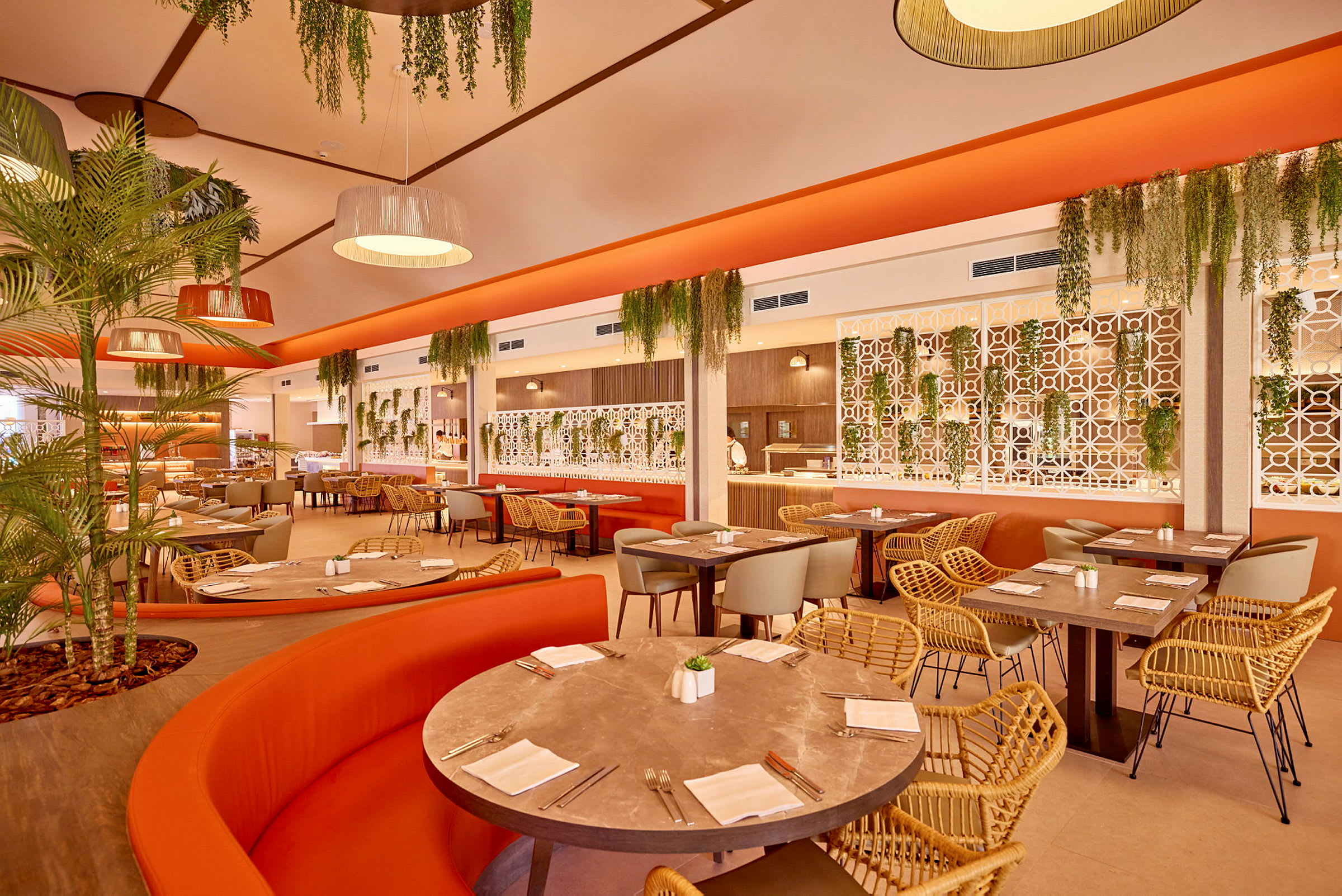 En restaurant med oransje sofaer, flettede stoler og grønne planter. (AI-generert tekst)