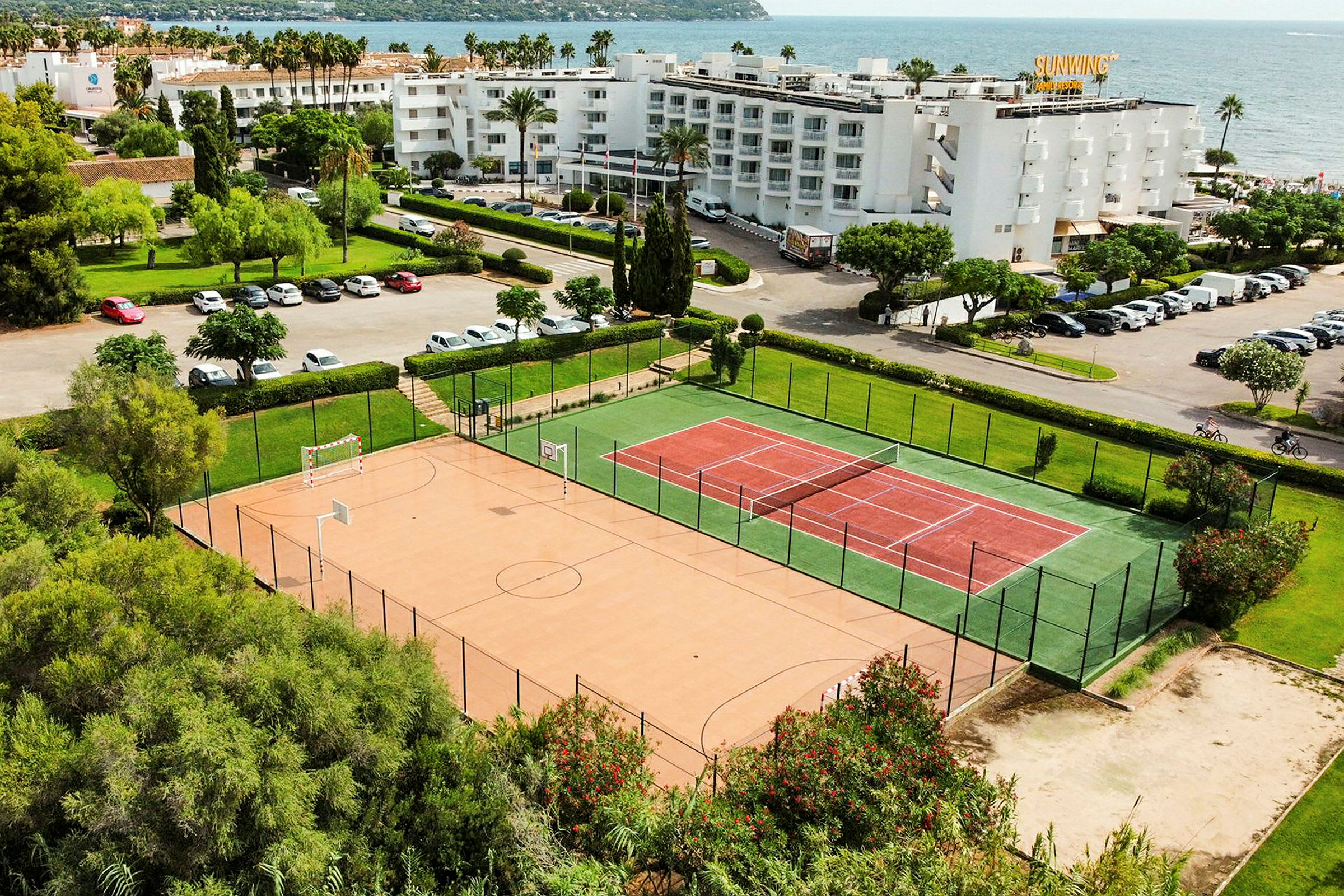 Bilde av et tennis- og sportsområde nær sjøen, med bygninger og parkeringsplasser i bakgrunnen. (AI-generert tekst)