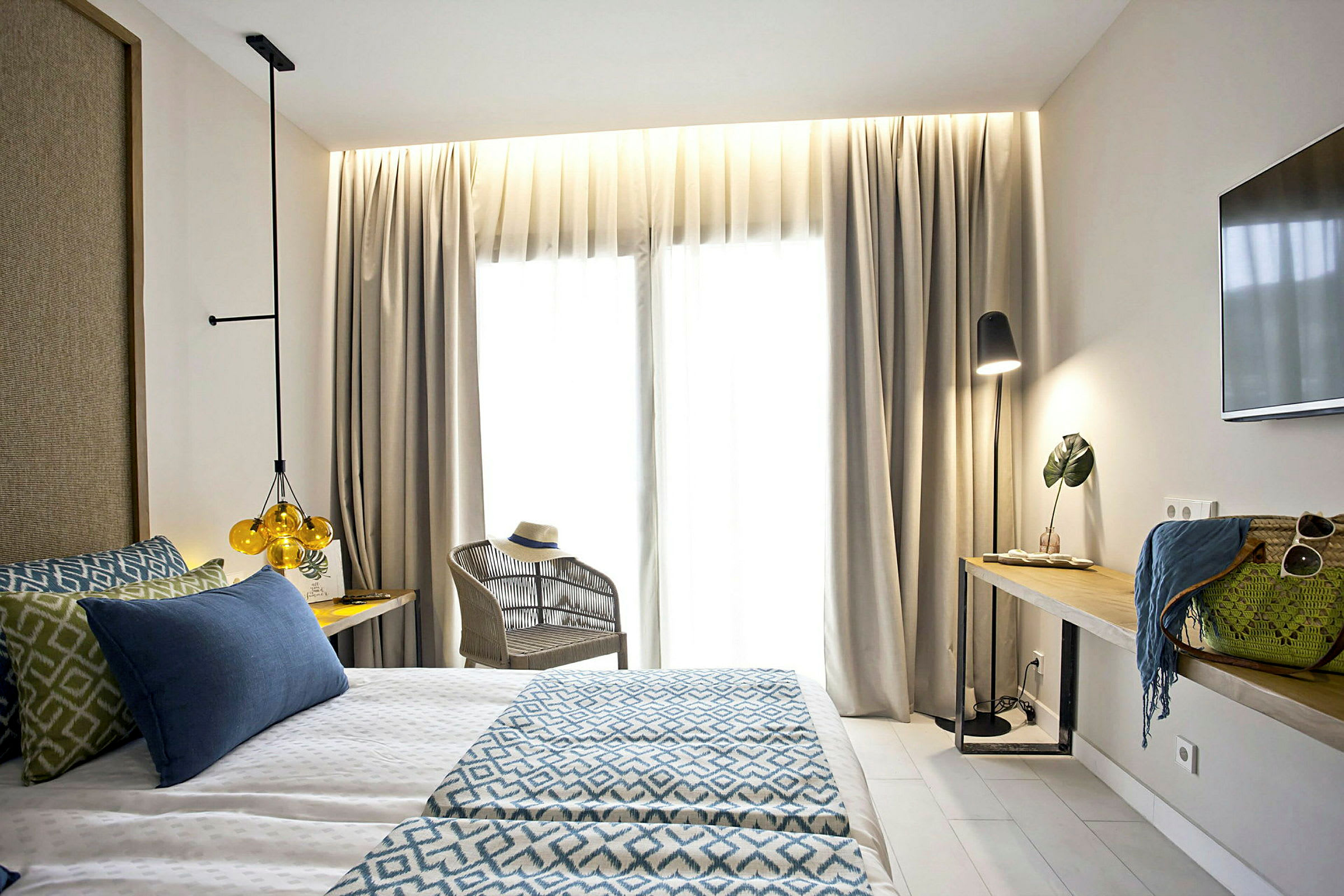 Et lyst hotellrom med en dobbeltseng, lenestol og et bord med dekorative gjenstander og lampe. (AI-generert tekst)