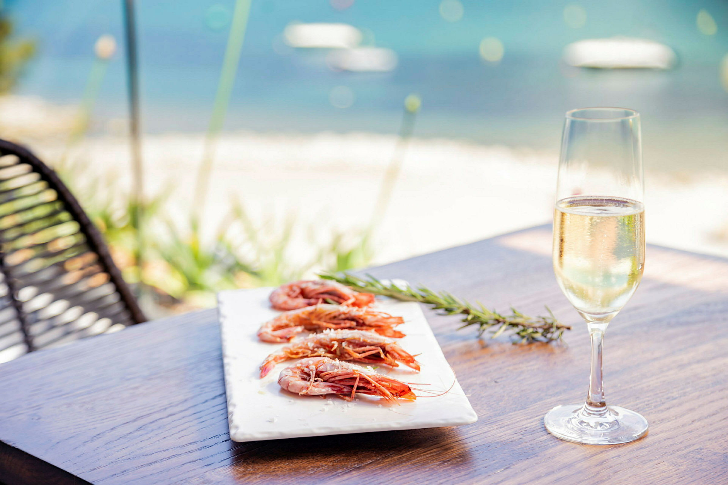 En tallerken med reker og et glass champagne på et bord ved sjøen. (AI-generert tekst)