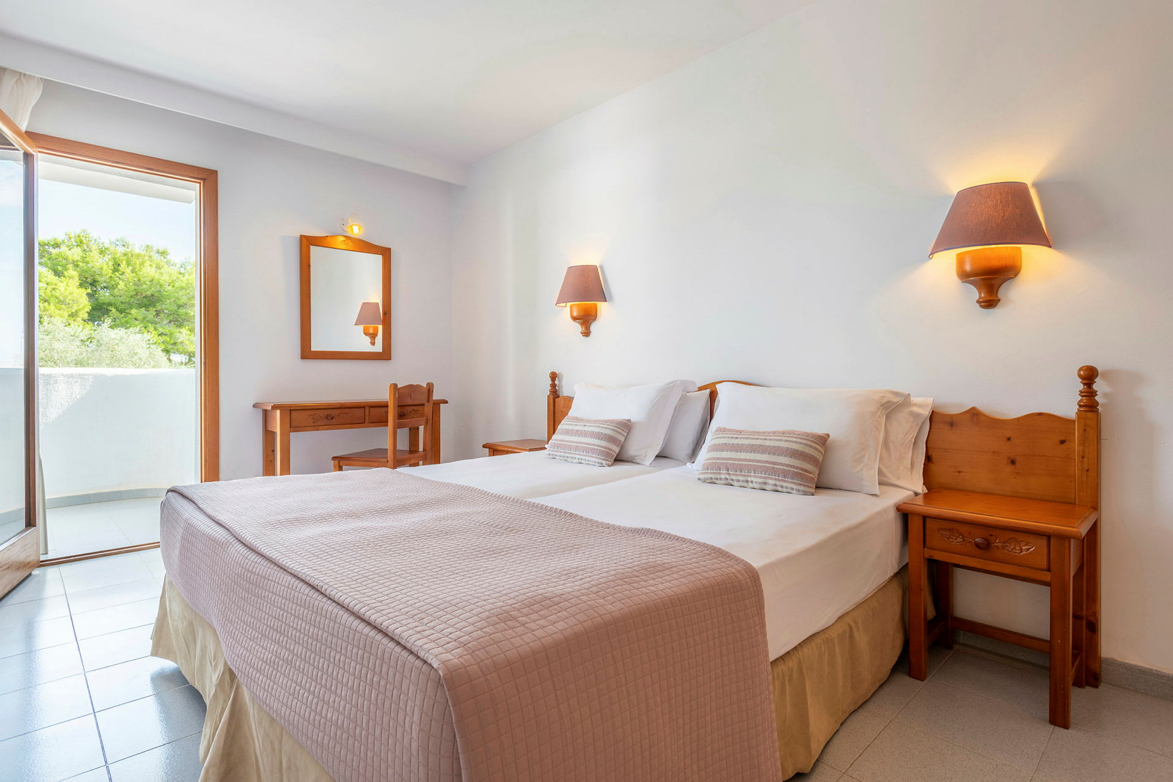 Et hotellrom med en dobbeltseng, to sengelamper, et skrivebord, en stol og en balkong. (AI-generert tekst)