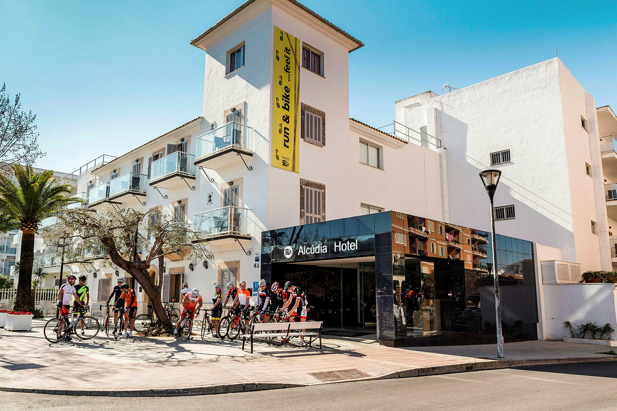 Utsikt over Alcudia Hotel med syklister samlet foran inngangen. (AI-generert tekst)