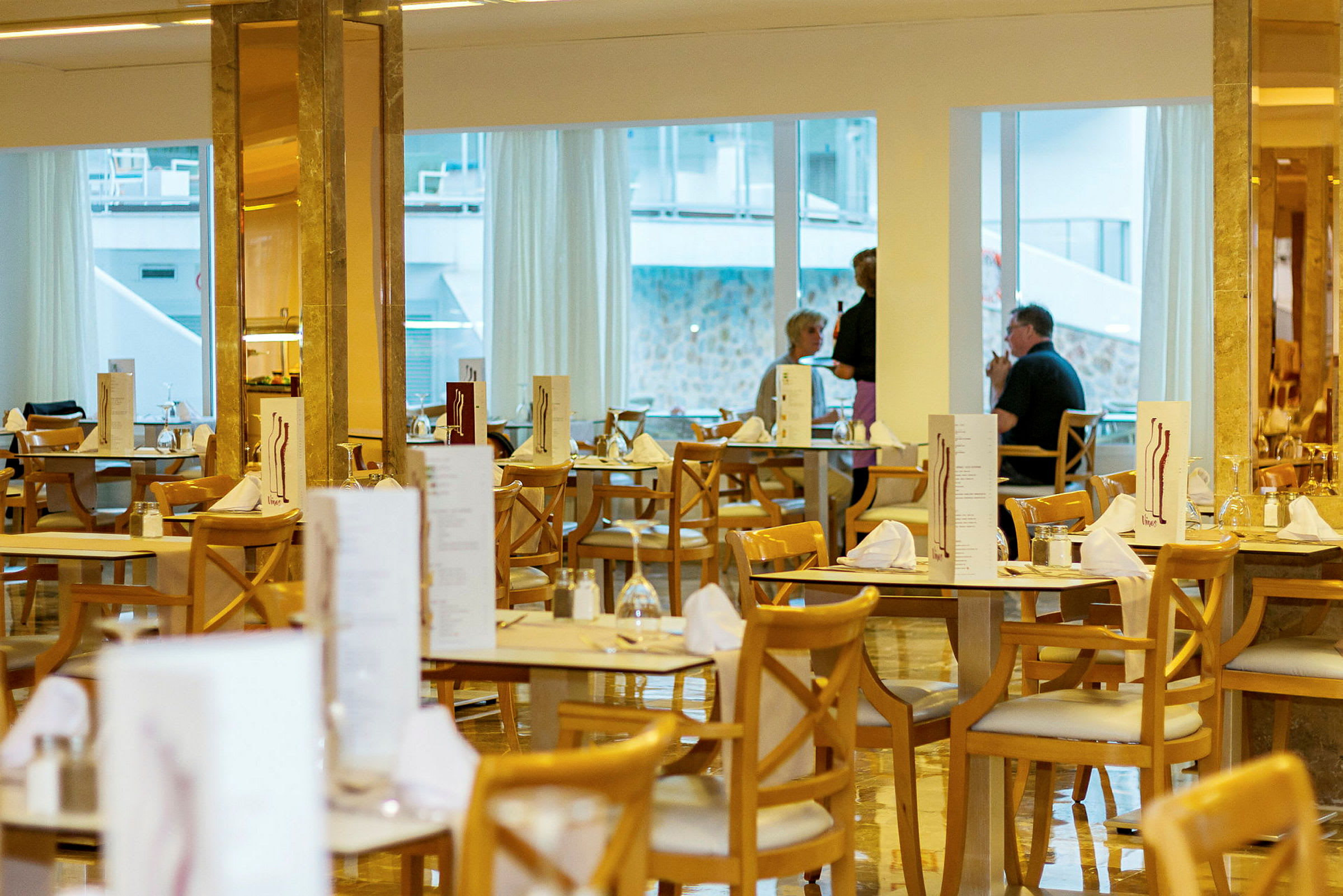 Restaurant med dukede bord og trestoler, vinduer i bakgrunnen. (AI-generert tekst)