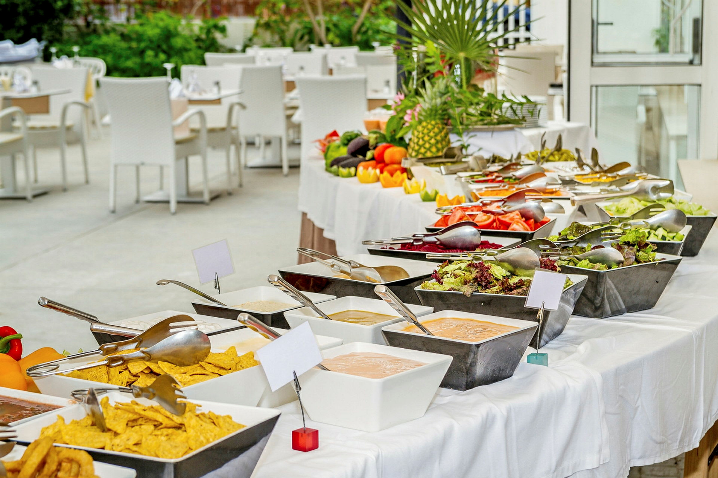 Buffet med salat, grønnsaker og sauser arrangert på et bord med hvite duker. Bak er det sitteplasser med hvite stoler. (AI-generert tekst)