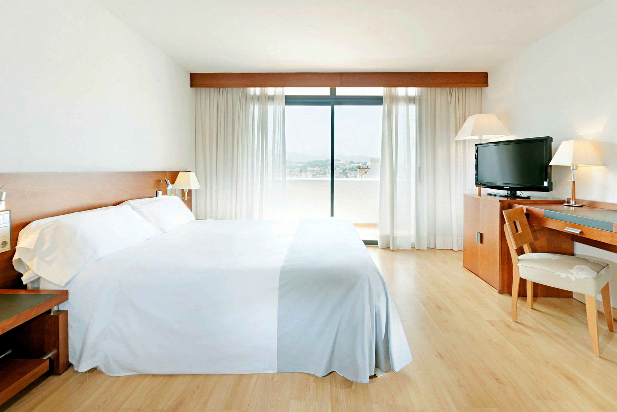 Hotellrom med en stor seng, skrivebord, stol, TV og et vindu med utsikt. (AI-generert tekst)