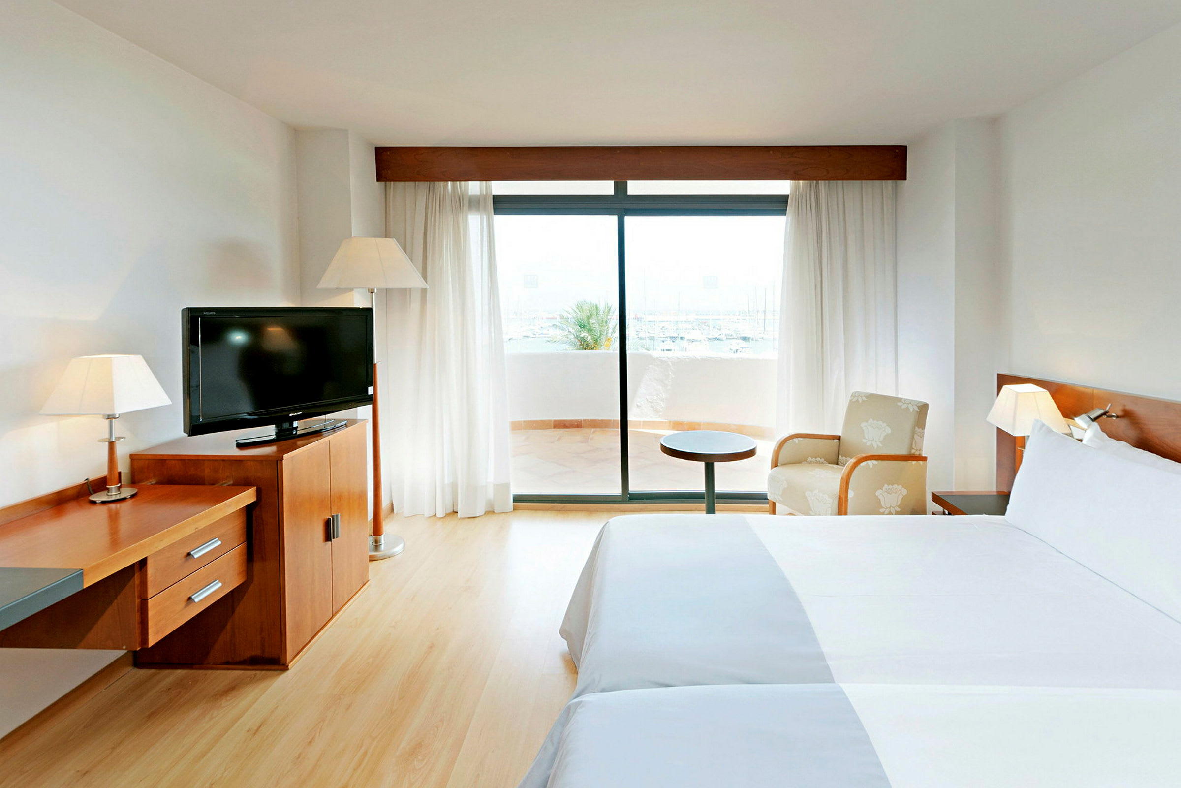Et hotellrom med to senger, en TV på en trekommode og en glassdør som fører ut til en terrasse. (AI-generert tekst)