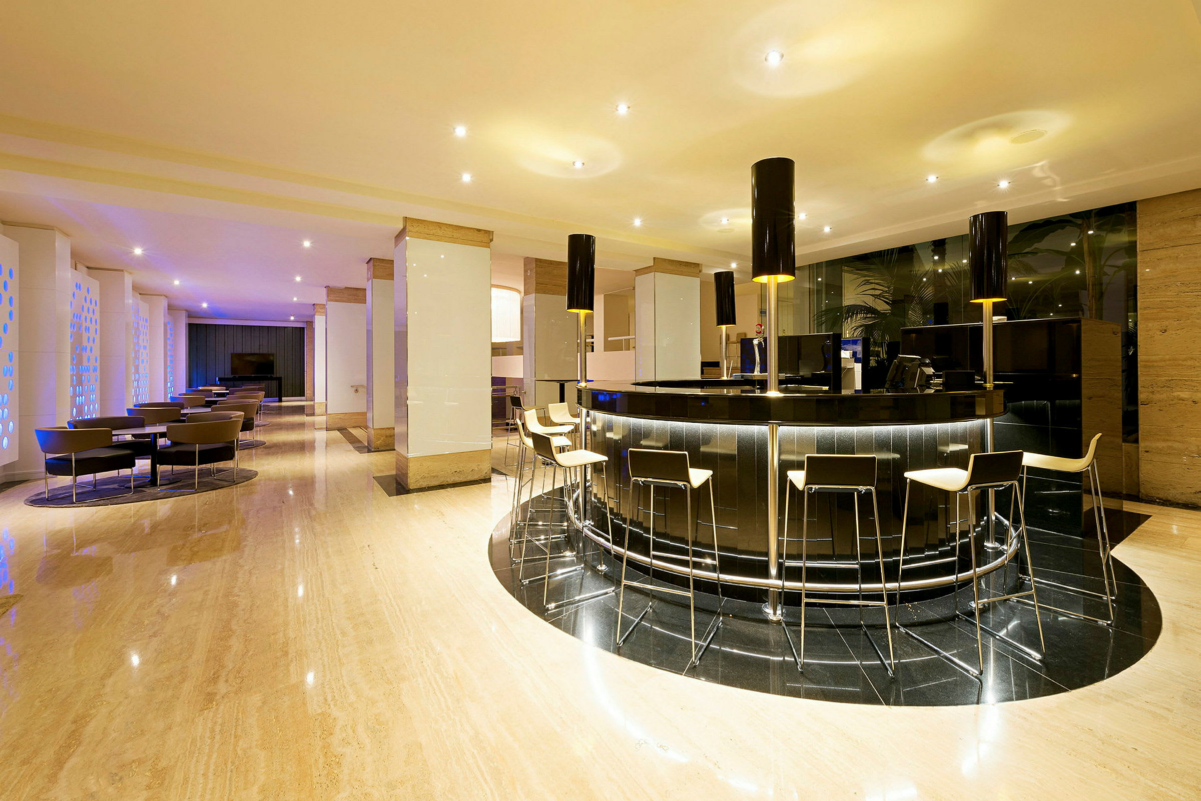 En moderne hotellobby med en elegant bardisk og barstoler. Det er stoler og bord plassert i bakgrunnen. (AI-generert tekst)