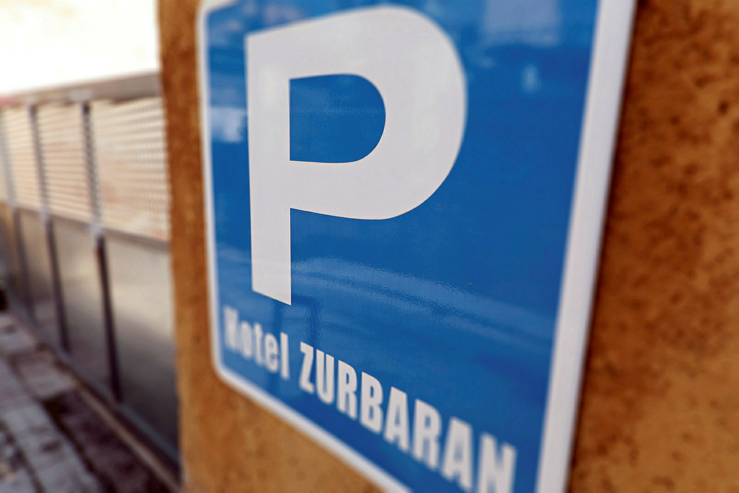 Et blått parkeringsskilt med teksten 'Hotel Zurbaran' som henger på en vegg. (AI-generert tekst)