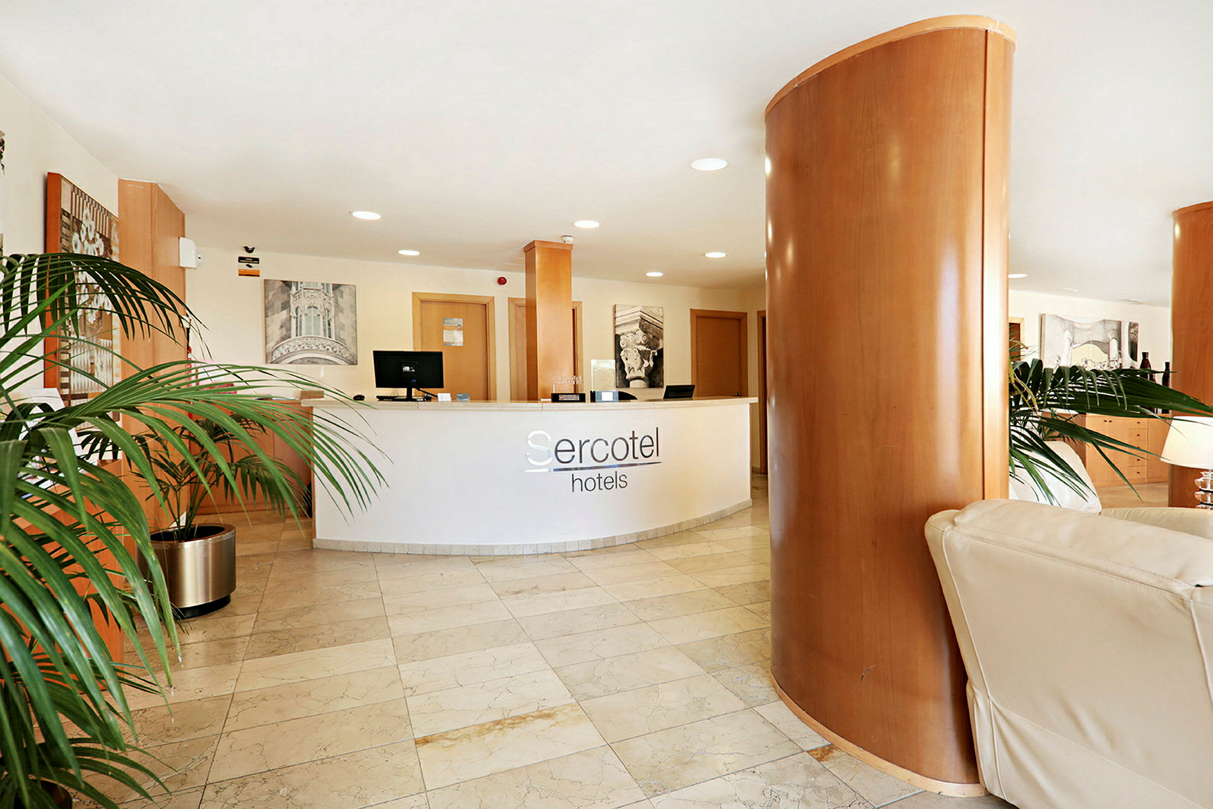 Resepsjonsdisken med hotell Sercotel-logoen vises i en lobby med marmorgulv og dekorative planter. (AI-generert tekst)