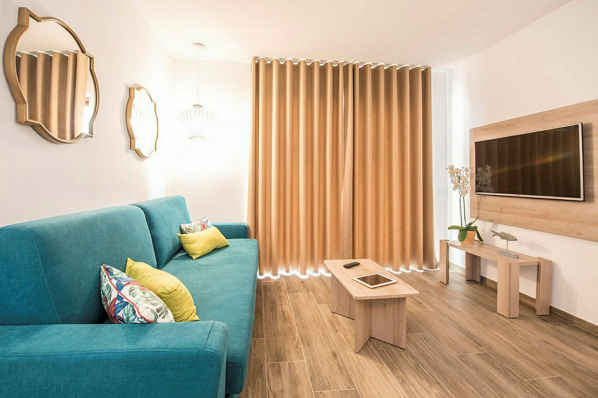 En moderne stue med en blå sofa, trebord, veggmontert TV og gardiner. (AI-generert tekst)
