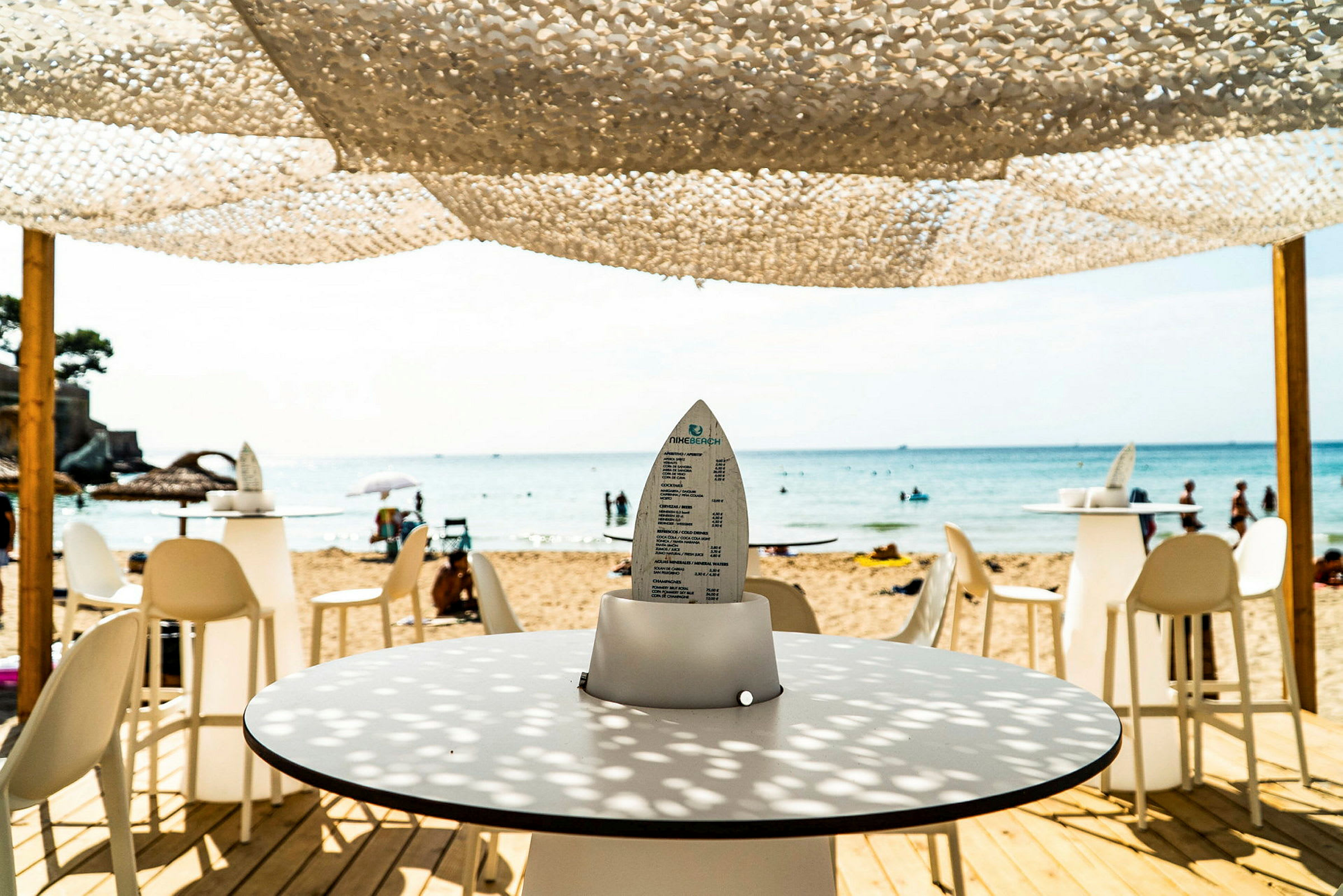 Utsikt fra en strandbar mot havet med bord og stoler. (AI-generert tekst)