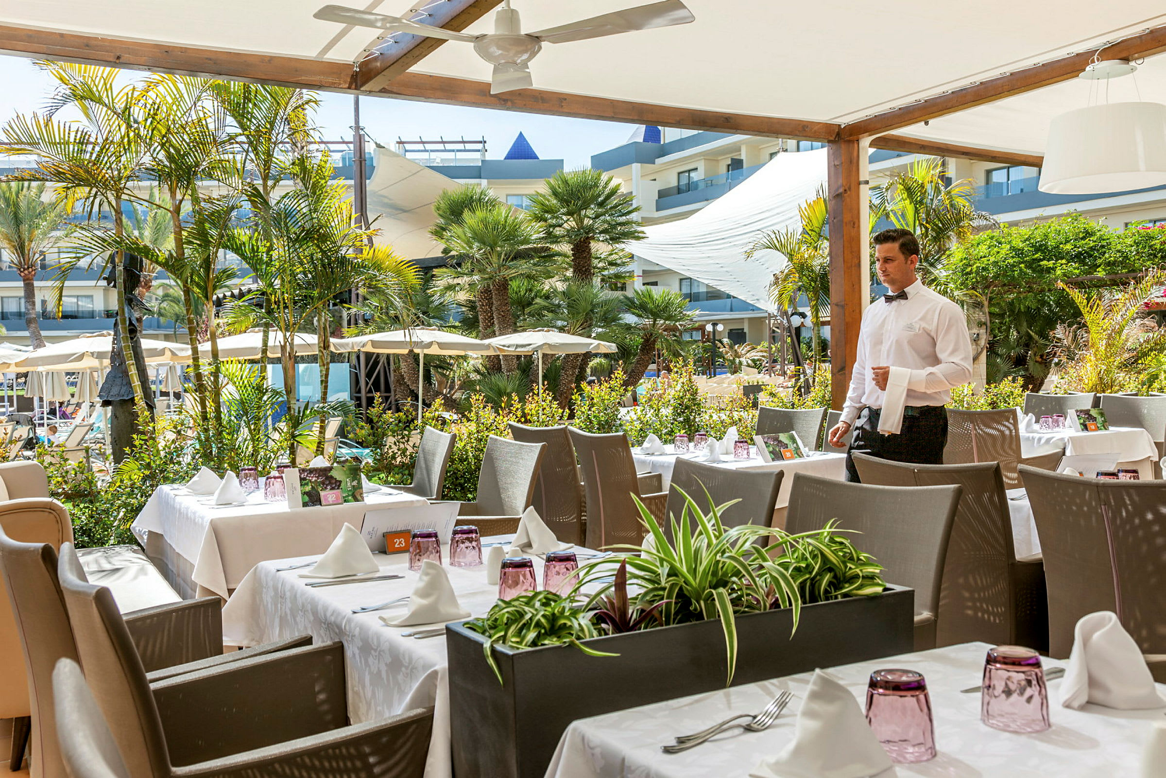 En utendørs restaurant med dekkede bord og en servitør i forgrunnen. (AI-generert tekst)