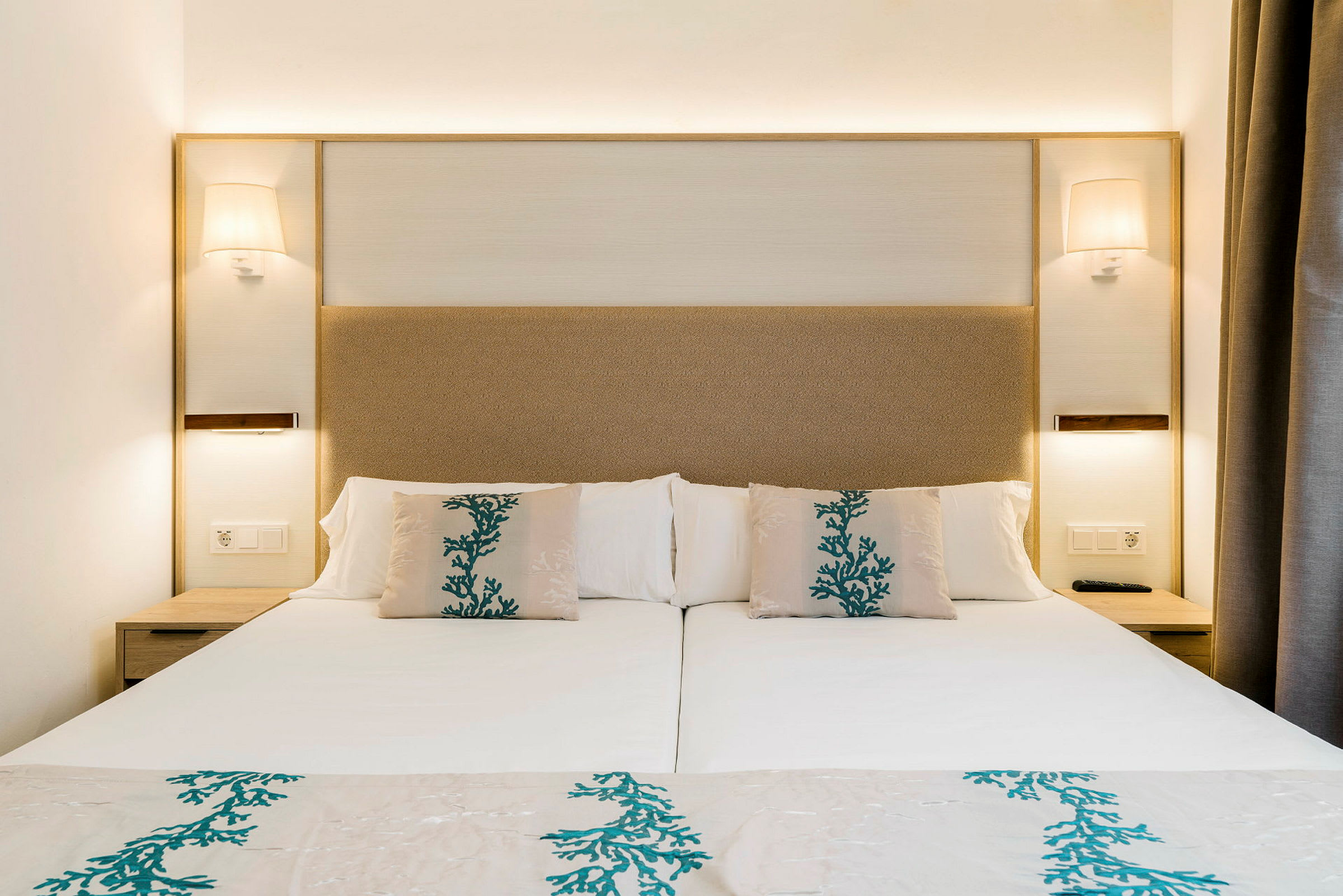 En hotellseng med hvitt sengetøy og puter dekorert med blågrønt mønster. (AI-generert tekst)