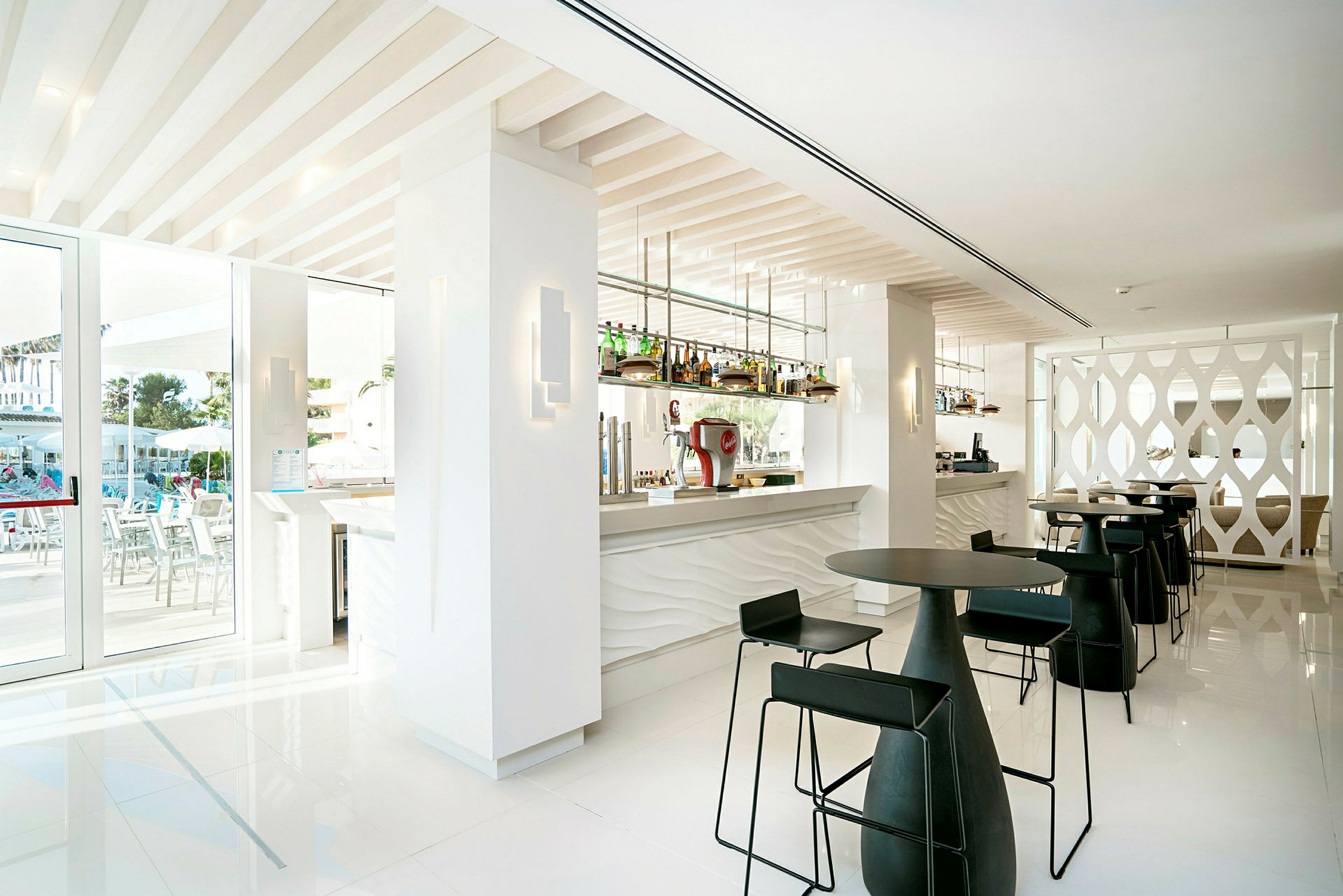 Et moderne hotellbarområde med hvite vegger, svarte stoler og en rad flasker ved bardisken. (AI-generert tekst)