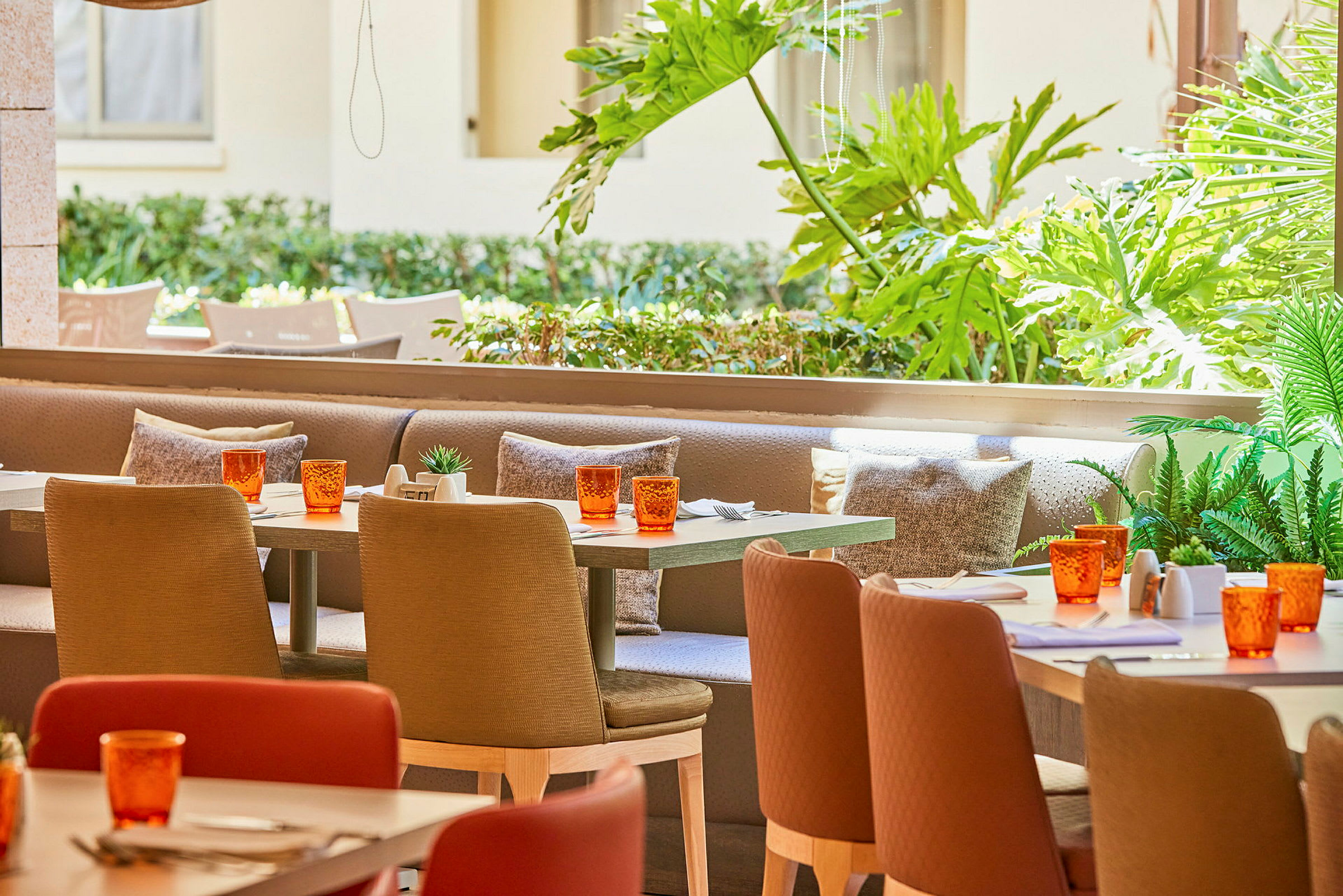 En kafé med uteservering, bord med oransje glass og sitteplasser med puter. (AI-generert tekst)