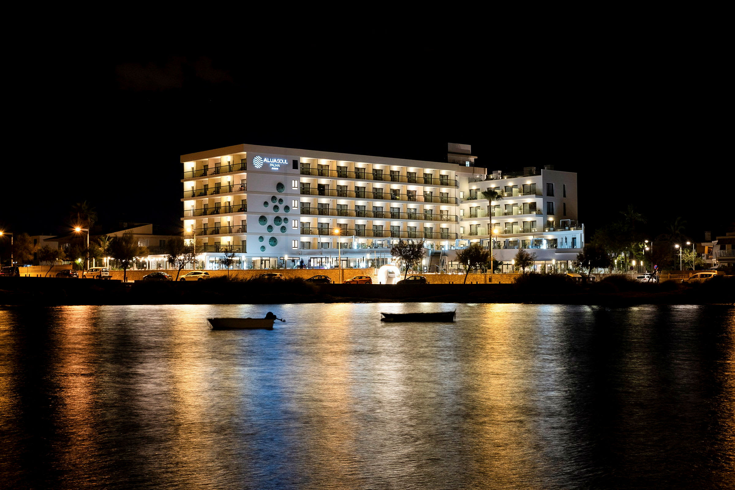 Hotellbygning med belyste balkonger ved vannet om kvelden. (AI-generert tekst)